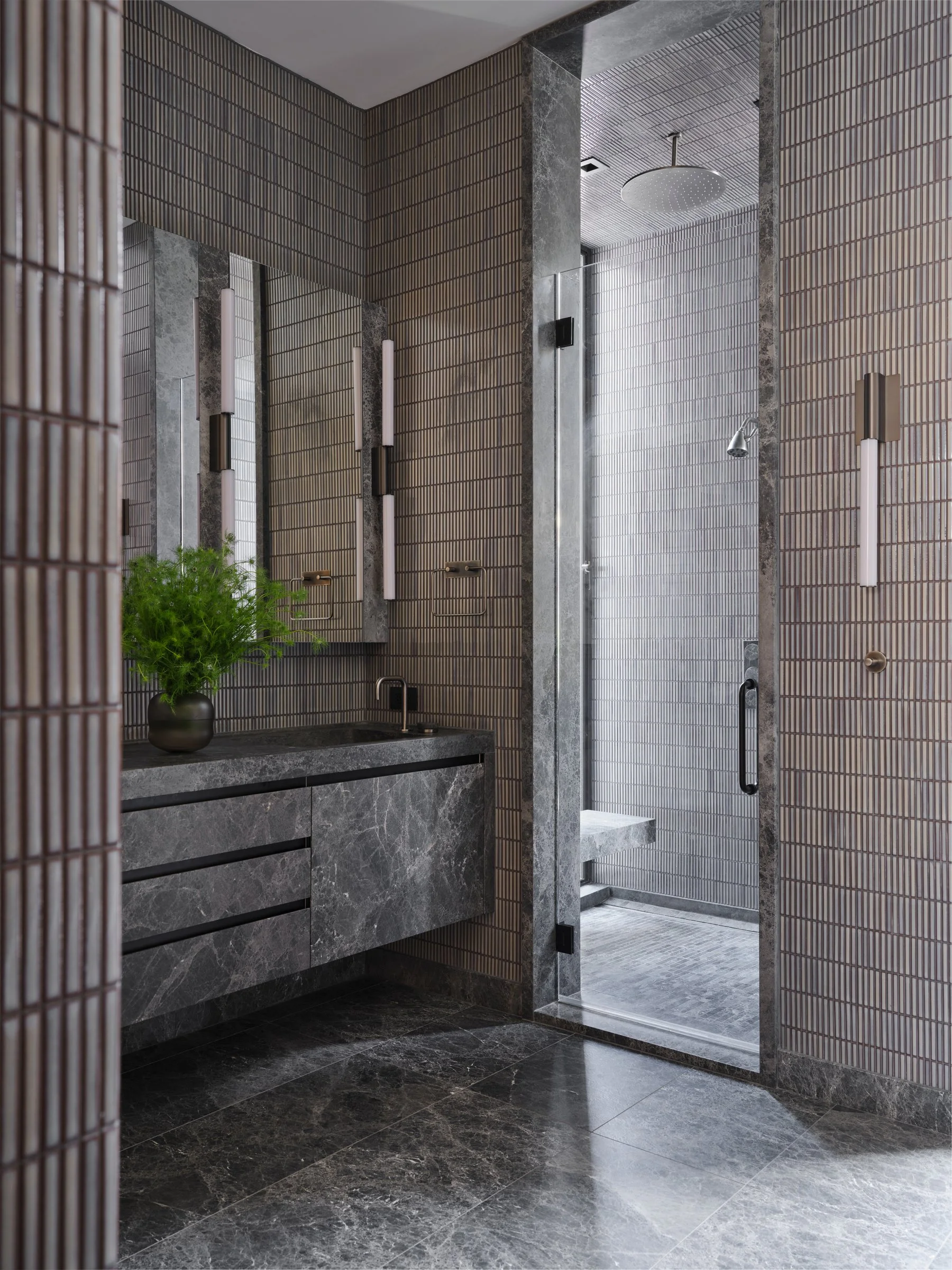 Modern luxury bathroom with stone vanity, textured tile walls, and glass-enclosed shower, emphasizing material depth and architectural detailing.