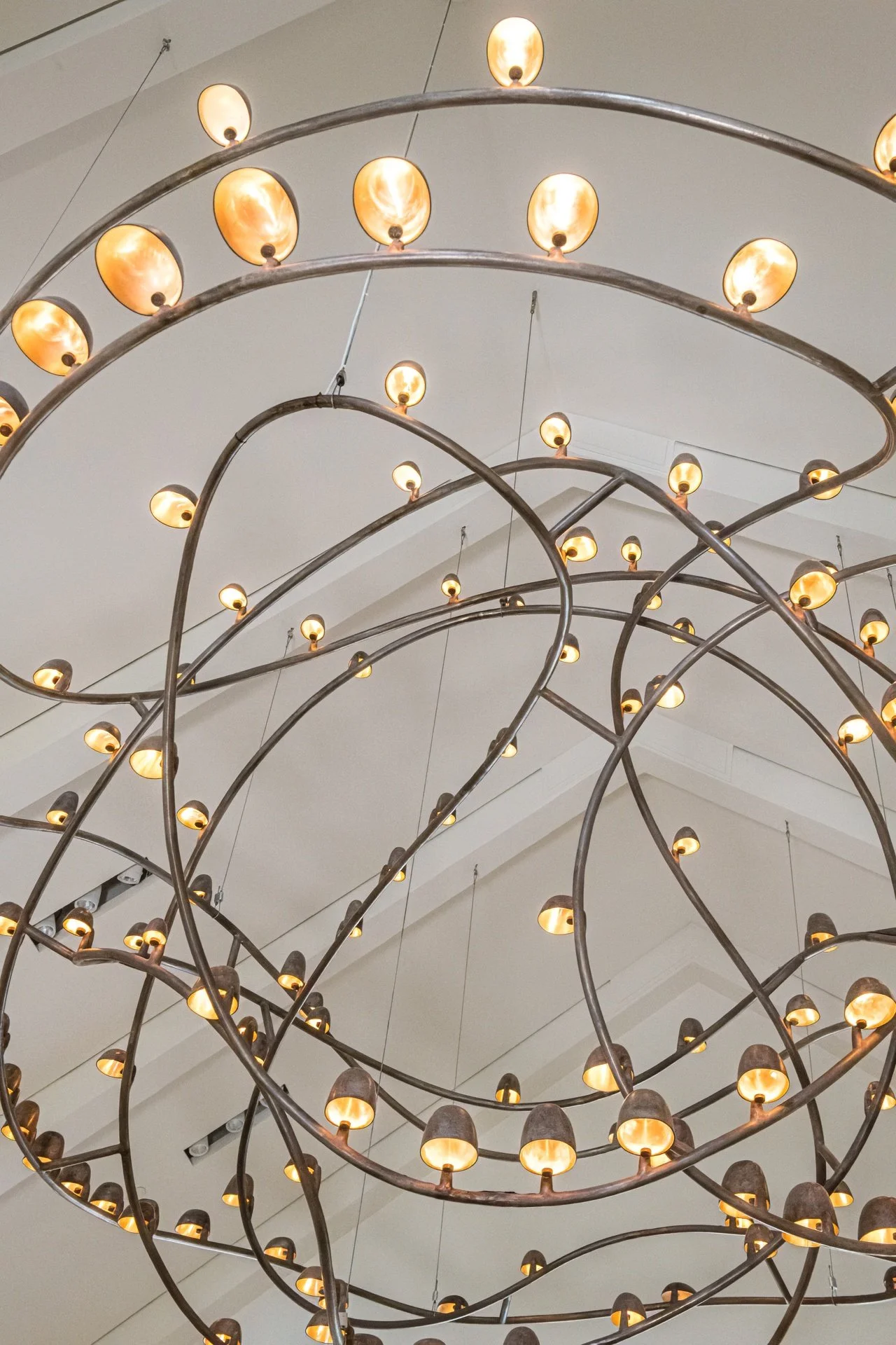 Sculptural suspended massive bronze chandelier by Frederik Molenschot with warm glowing lights suspended beneath vaulted ceilings in a dramatic modern great room.