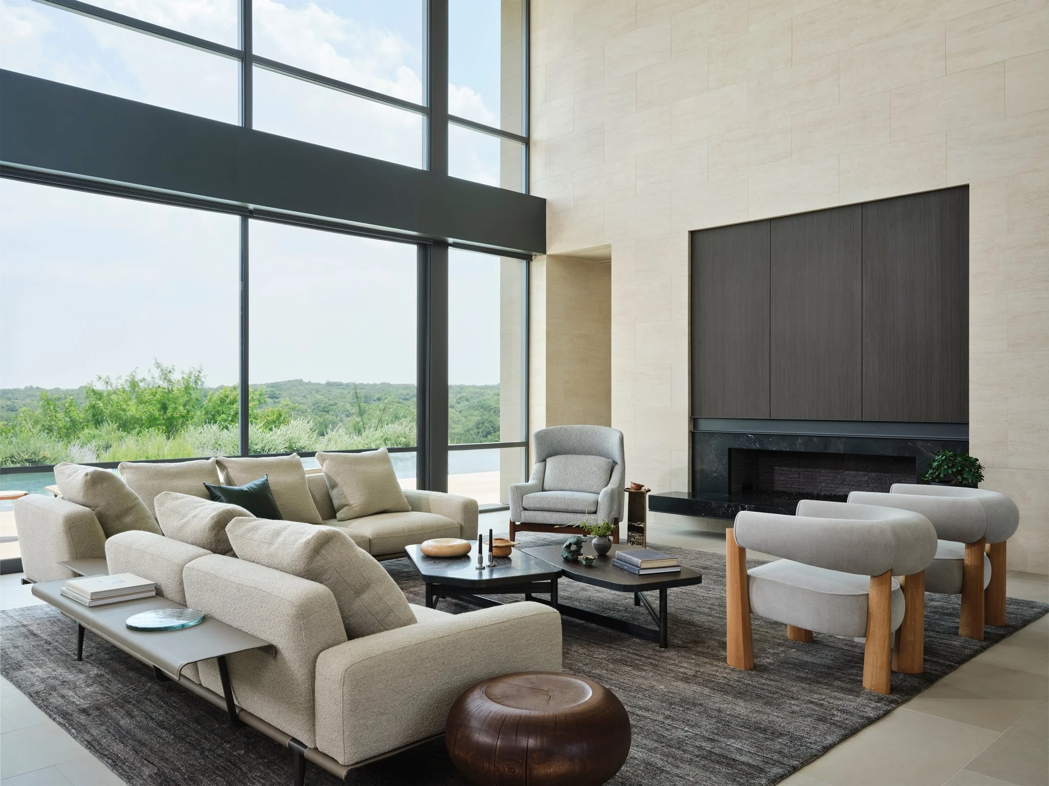 Minimal living room with low modern sofas, sculptural wood stools, and expansive glass walls overlooking the Texas Hill Country landscape. Poltrona frau, keiran kinsella, maxime boutillier chair by jens risom