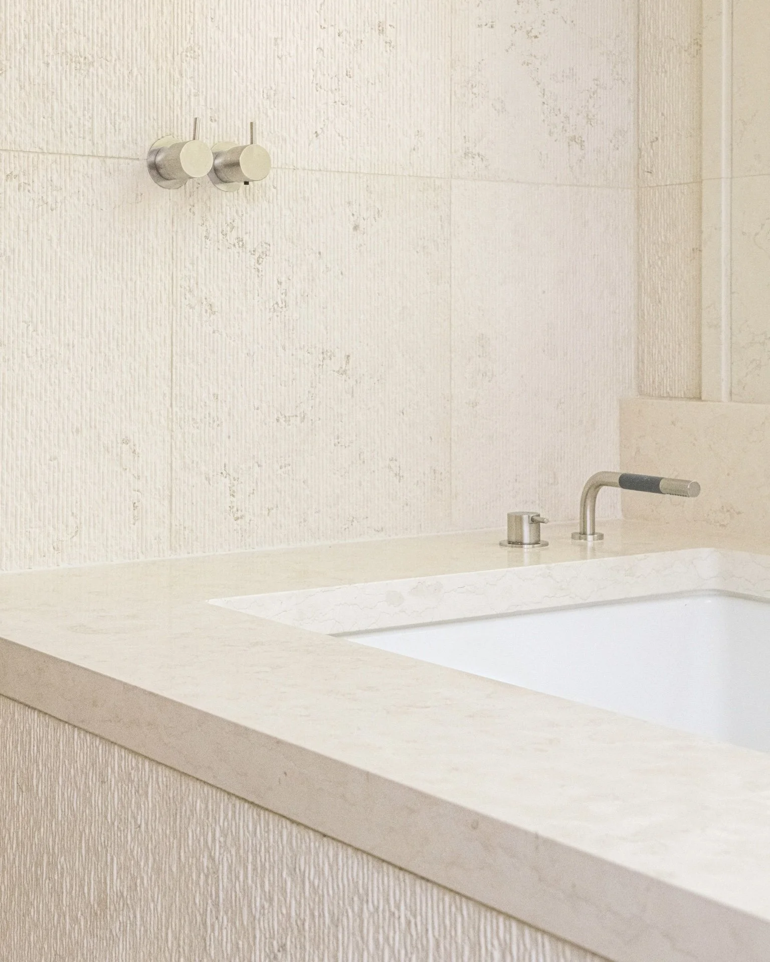 Textured stone bathroom with integrated bathtub, brushed metal faucet, and minimalist detailing in a refined modern luxury residence.