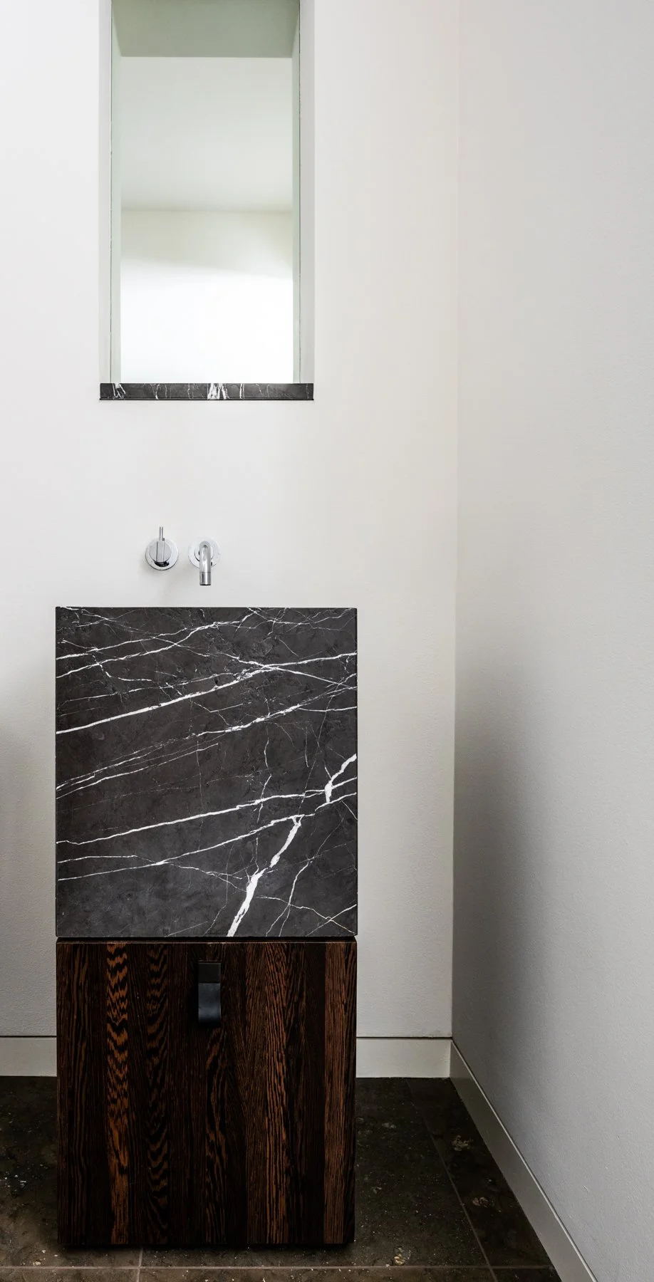 Modern powder room with sculptural marble sink, wall mounted chrome faucet, and dark solid wenge wood cabinet minimalist bath