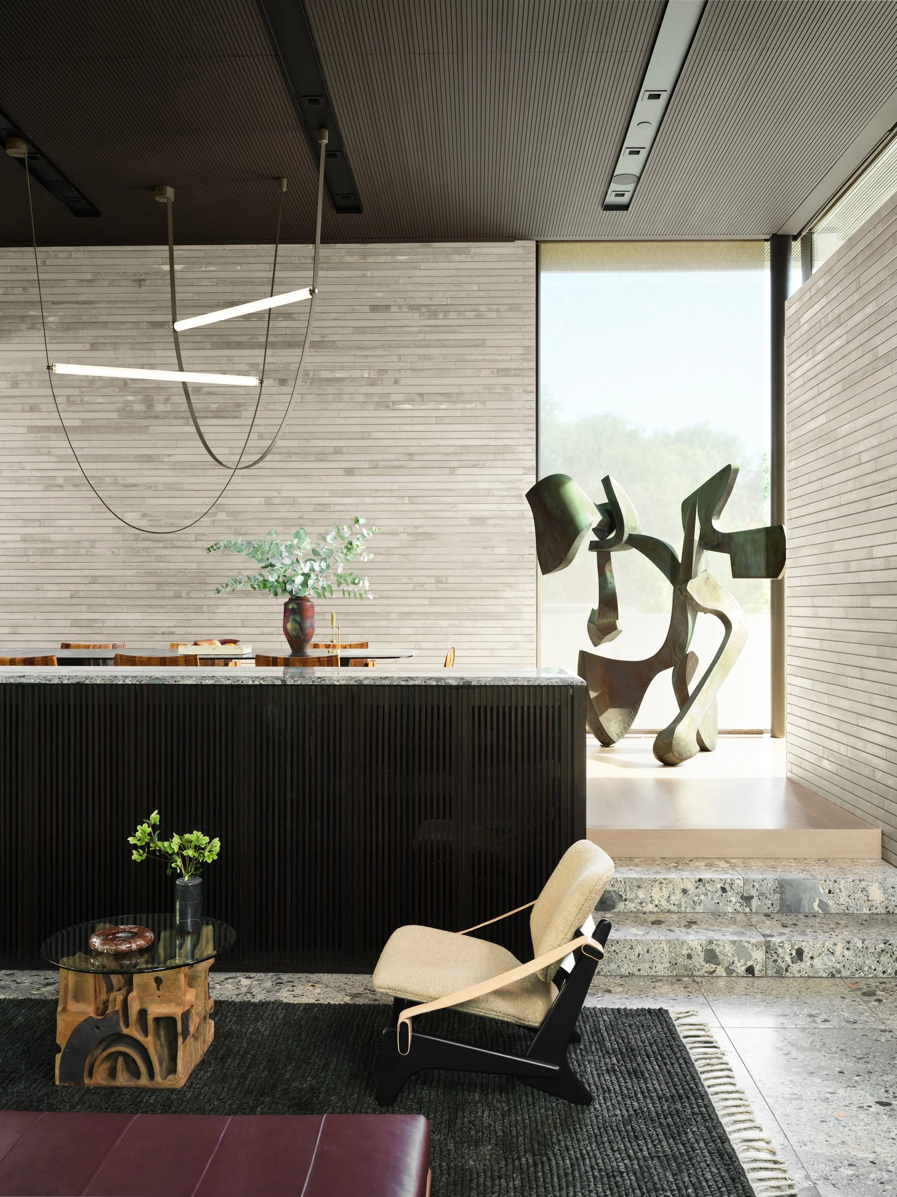 Dining and bar area with fluted millwork and ceppo marble surfaces, anchored by large-scale abstract sculpture by Bill Barrett and controlled natural light.