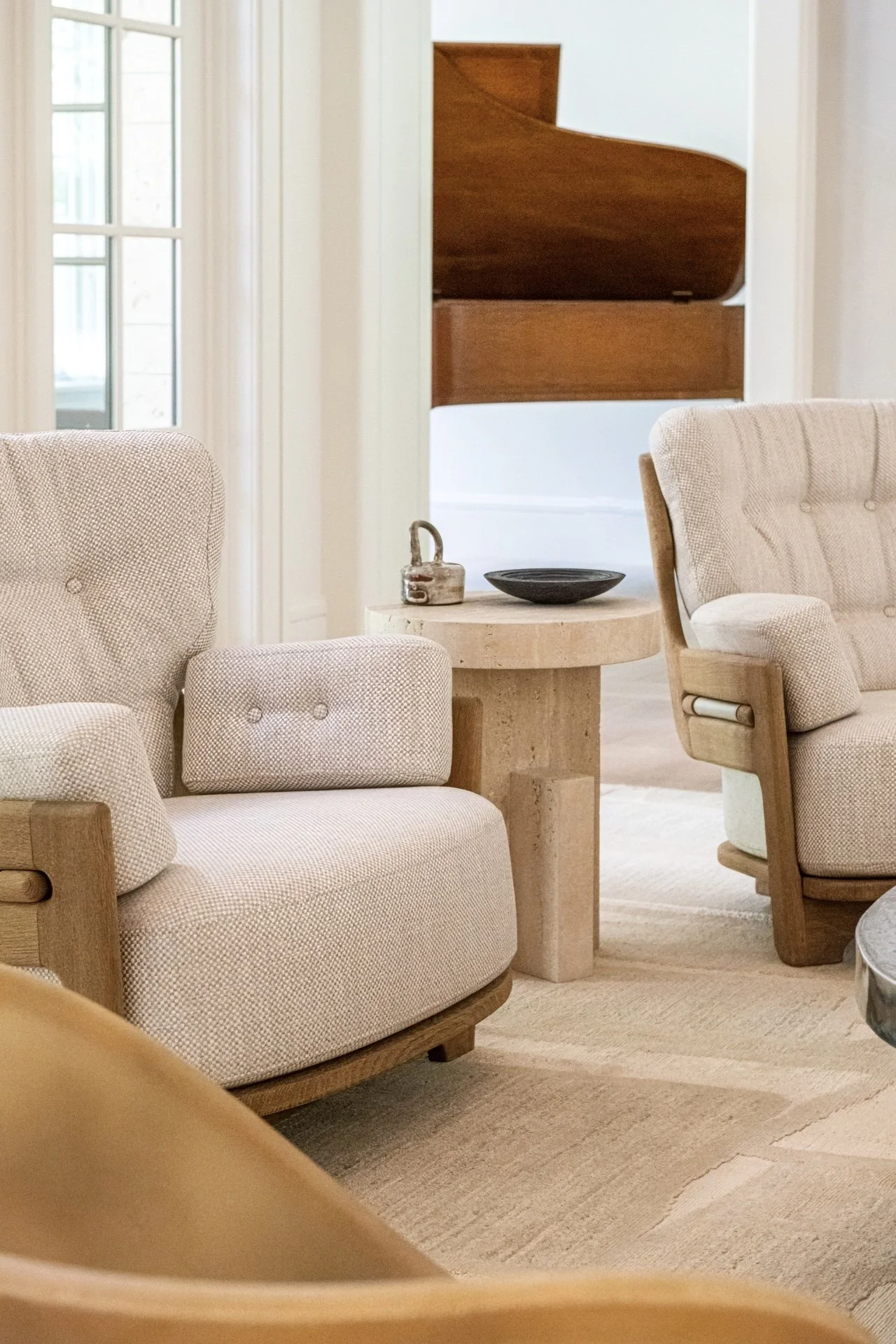 Lounge chairs by Faye Toogood and guillerme et chambron and stone pedestal side table by Fort Standard vignette with grand piano backdrop in a quiet, curated luxury residential interior.