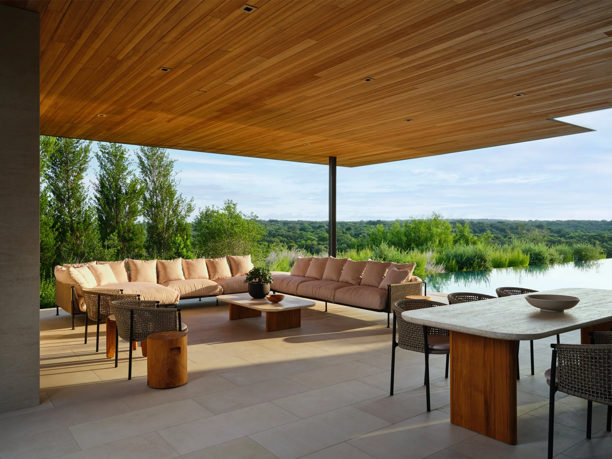 Covered outdoor terrace overlooking the Texas Hill Country with wood soffit ceiling, infinity-edge pool, and modern outdoor lounge and dining areas designed for seamless indoor-outdoor living. jader almeida and harbour outdoor furniture