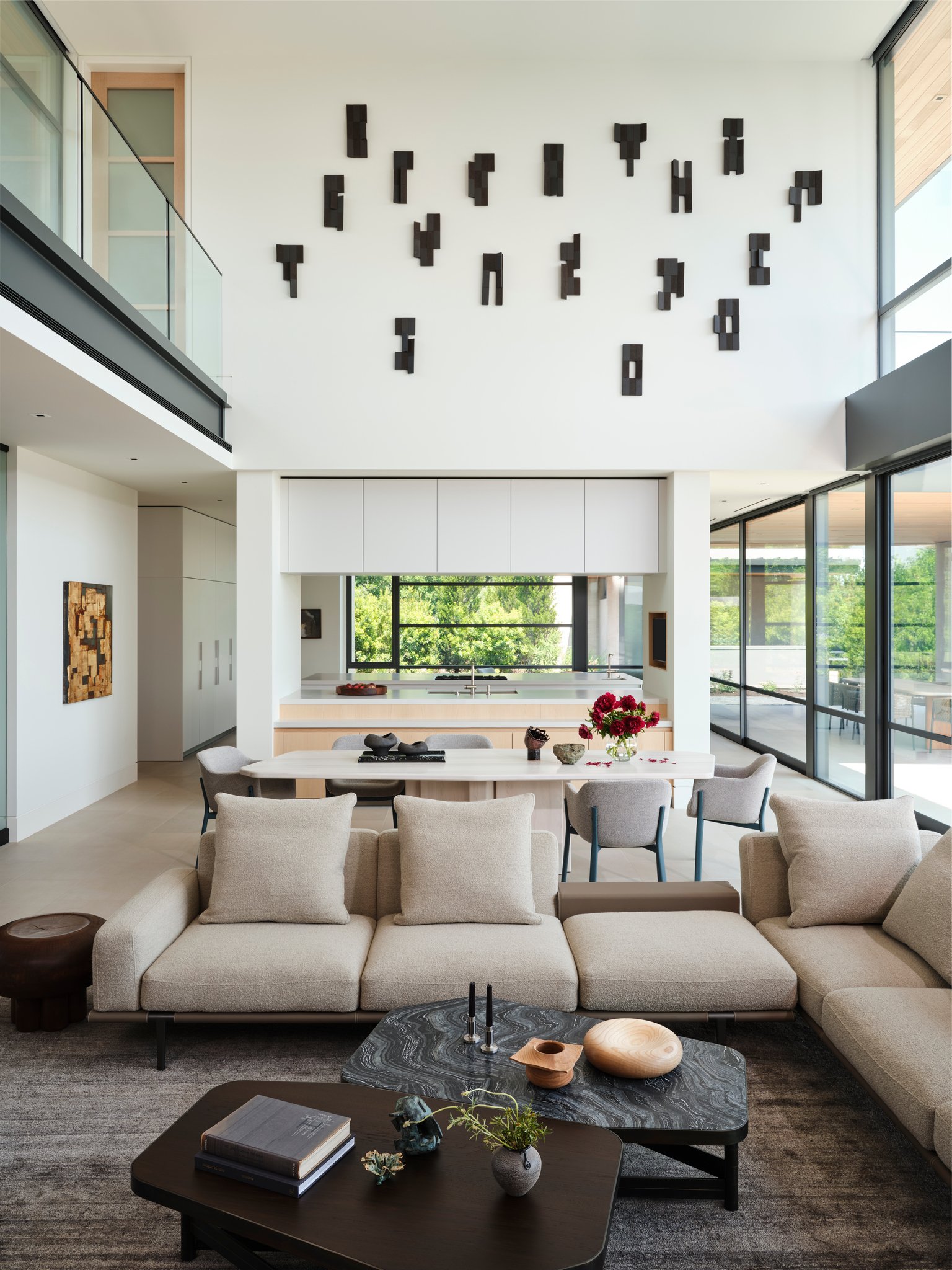 Open living room with sectional seating, sculptural coffee tables, and views toward the dining area and kitchen. A tall gallery wall features a contemporary art installation.  henge, poltrona frau, denis castaing, bulthaup