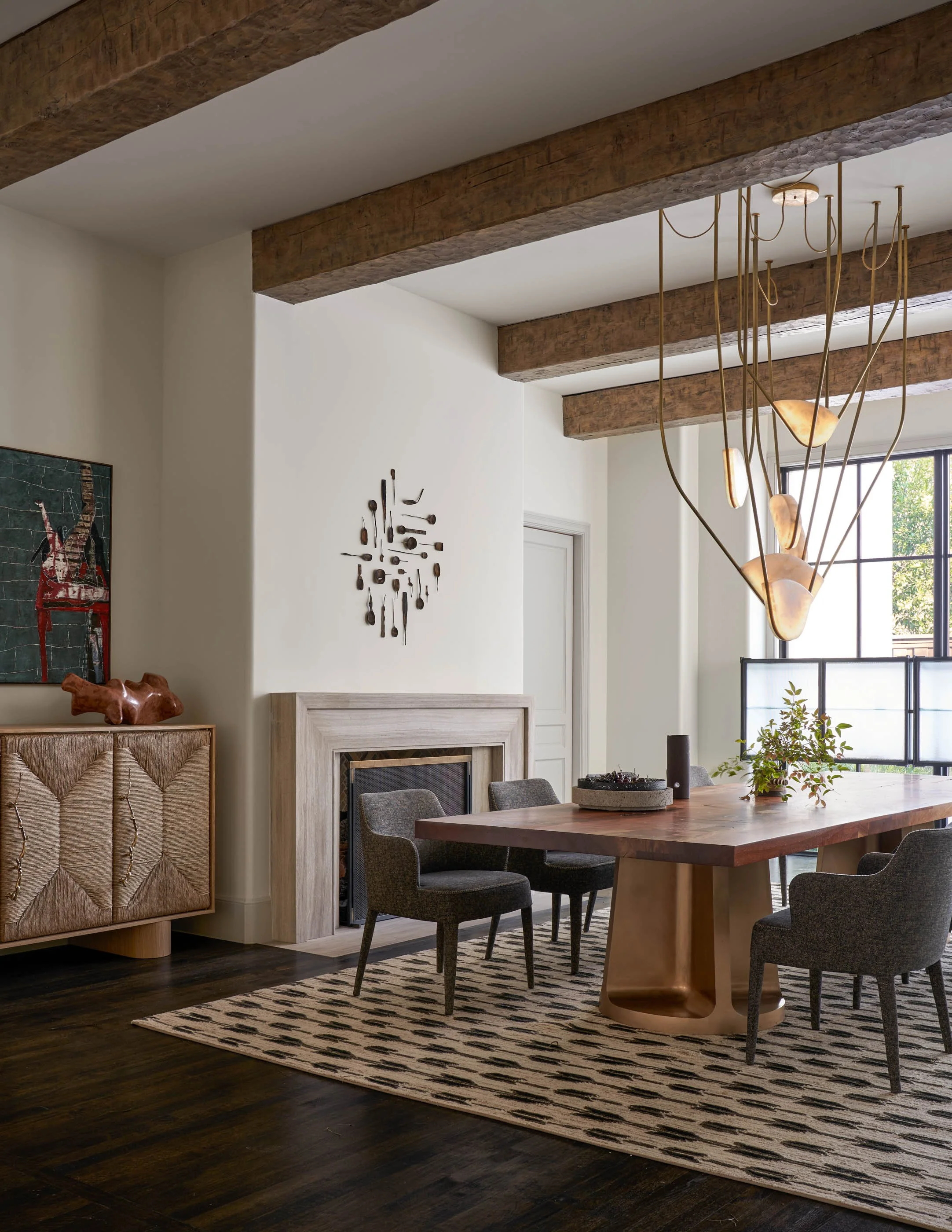 Moody and warm dining room with custom wood dining table, sculptural brass chandelier, and contemporary artwork