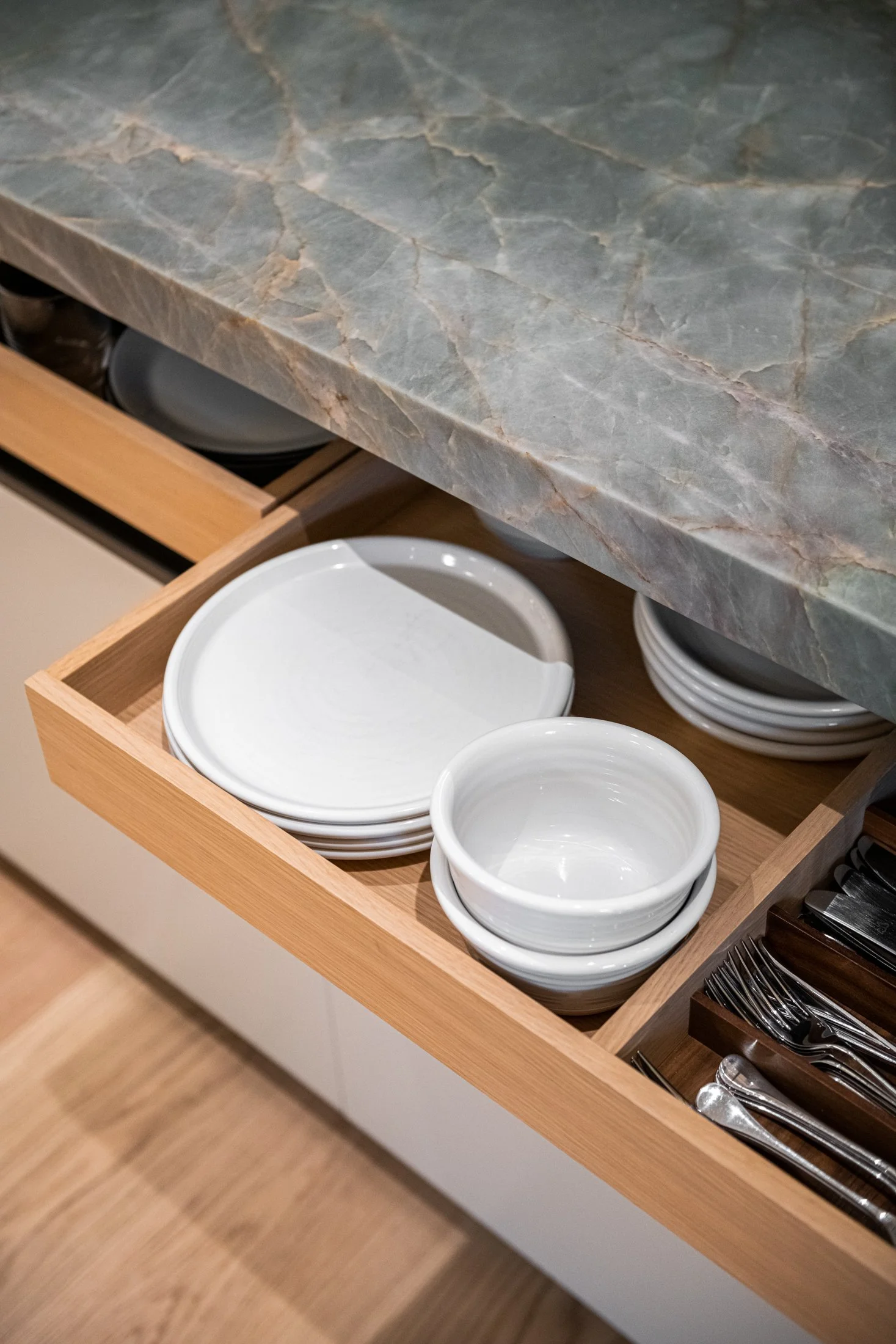 Stone countertop detail with custom oak drawer storage, organized tableware, and refined kitchen millwork in a high-end residential interior.