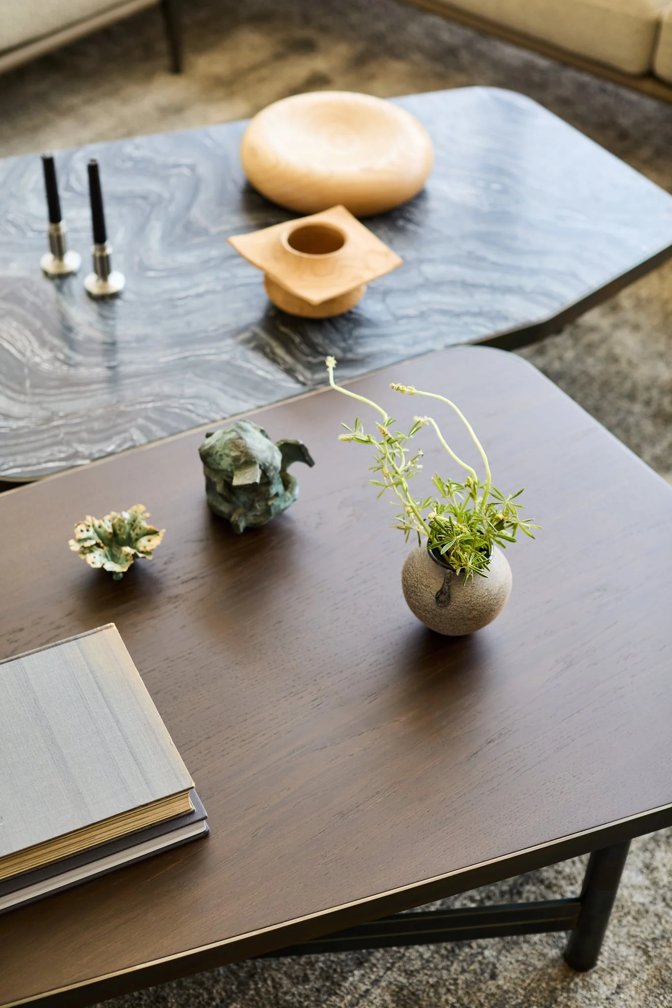 Layered henge coffee tables in wood and stone styled with ceramic vessels and small sculptural objects within a calm contemporary living room setting.