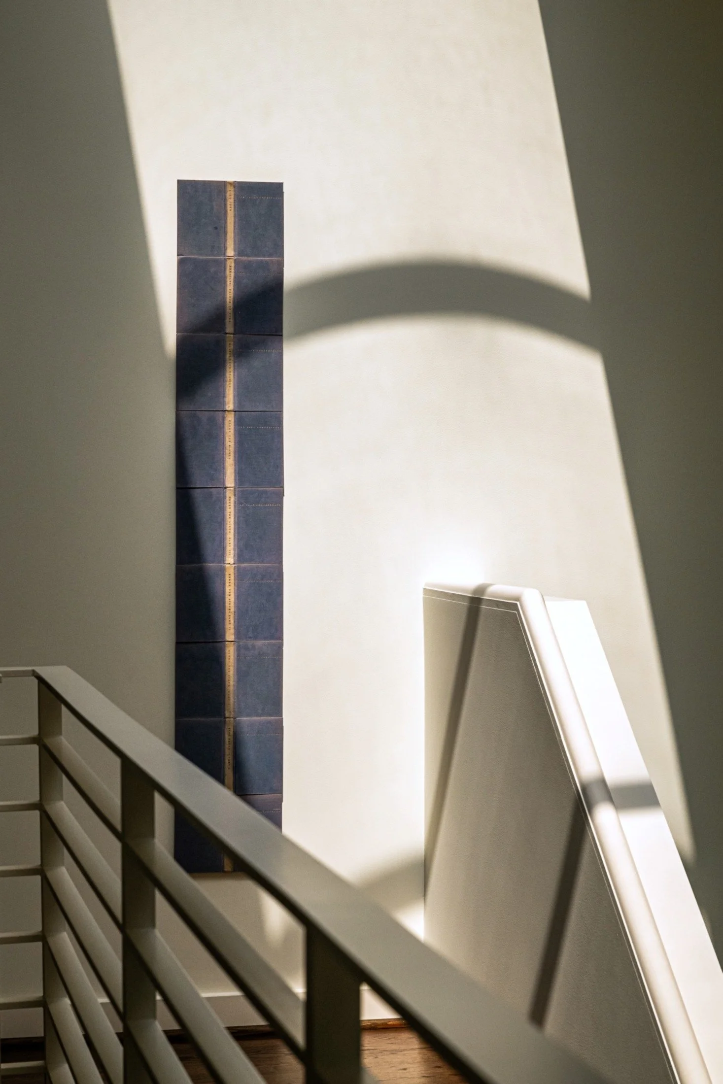 Modern staircase with strong natural light casting shadows across plaster walls and sculptural wall art elements, highlighting architectural interior design.