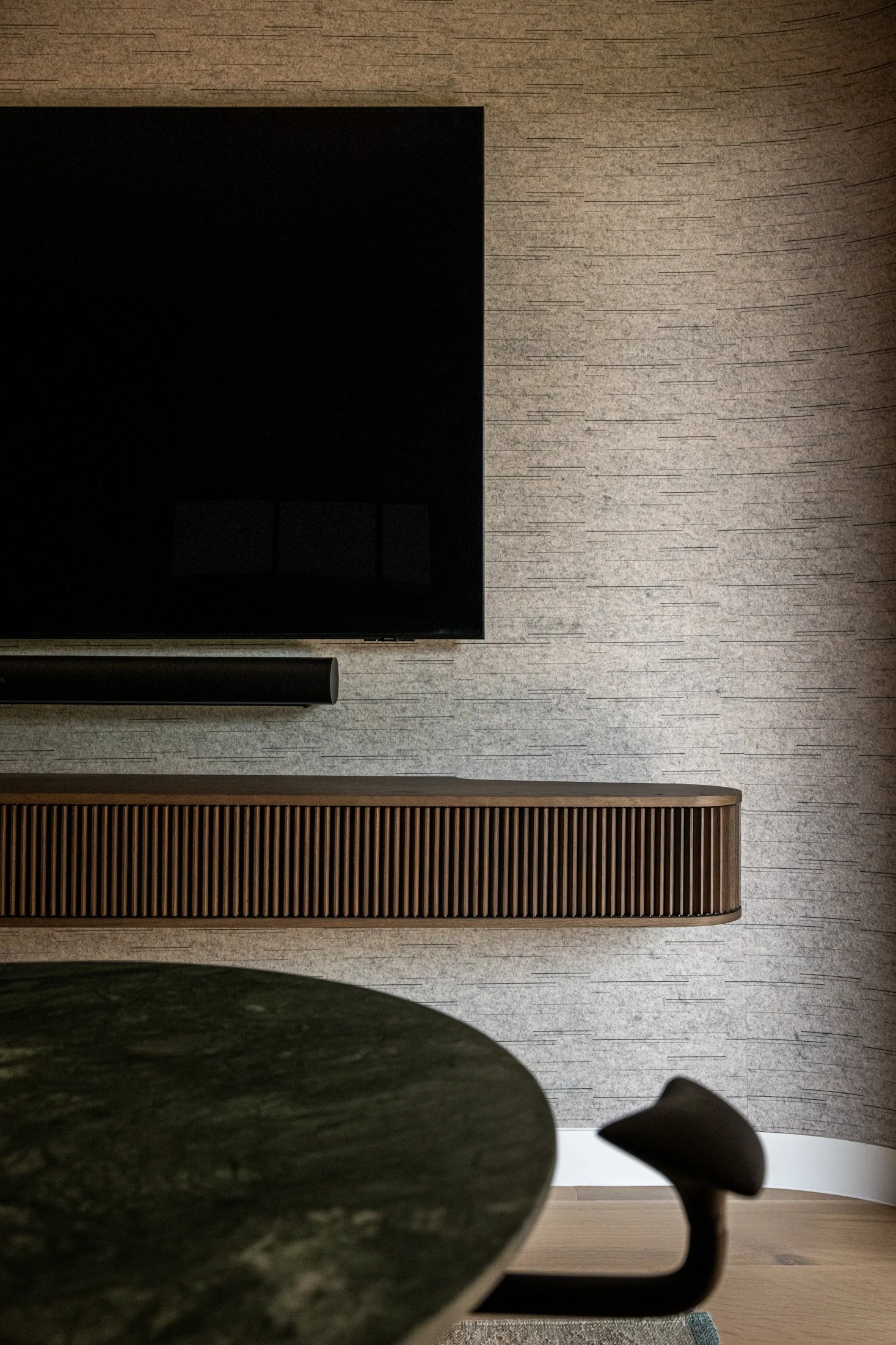 Curved wood media console by jader almeida with fluted detailing beneath wall-mounted display, emphasizing proportion and integrated millwork.