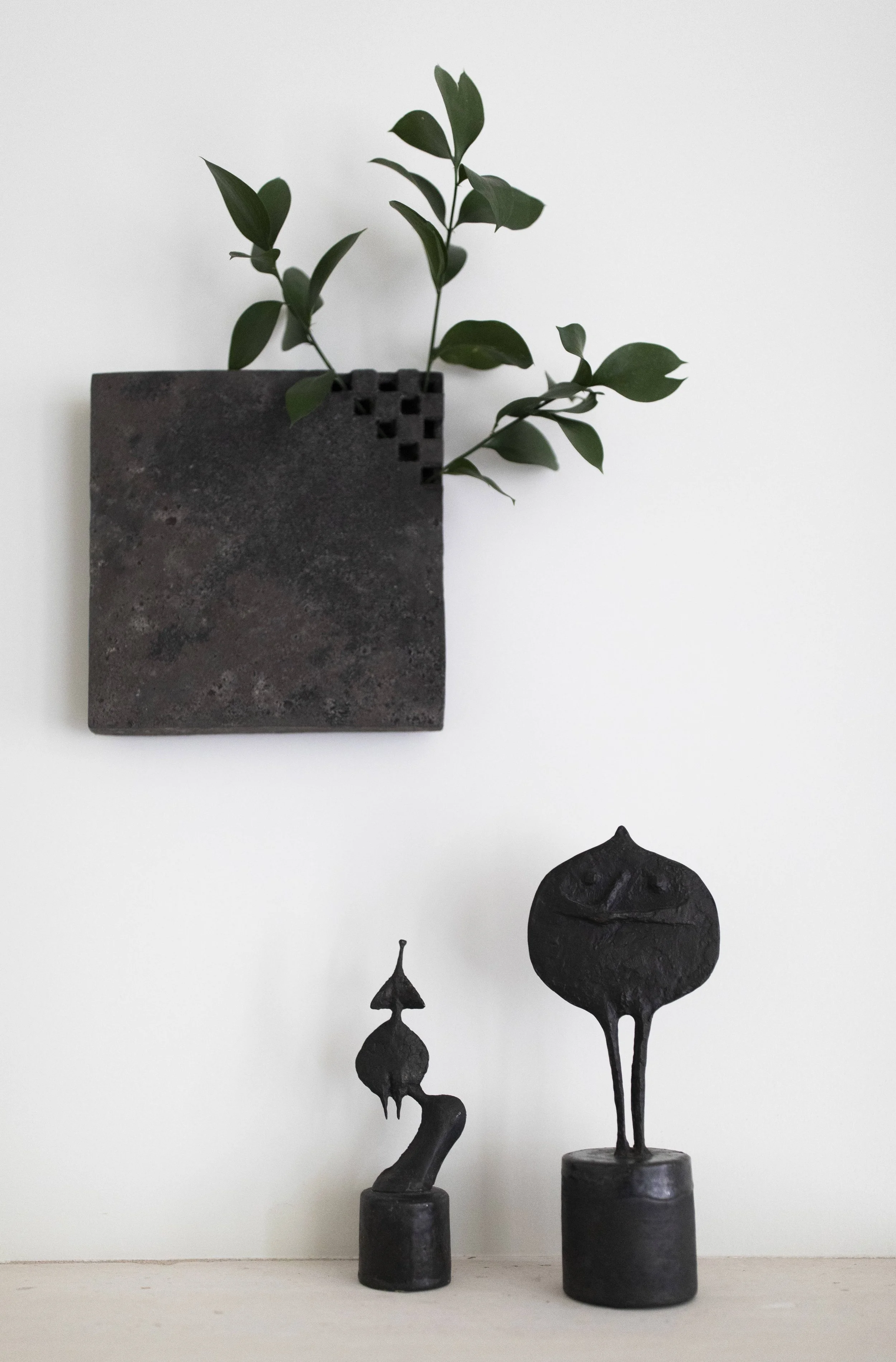 Minimal wall mounted metal planter with greenery above small abstract bronze sculptures ruth duckworth japanese vase