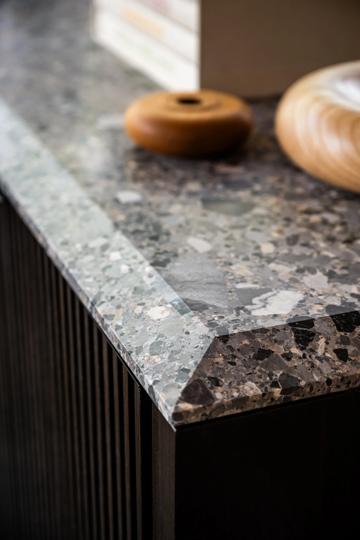Custom grey ceppo de gris countertop with mitered edge over dark wood millwork, highlighting material contrast and precise detailing in a modern luxury interior.