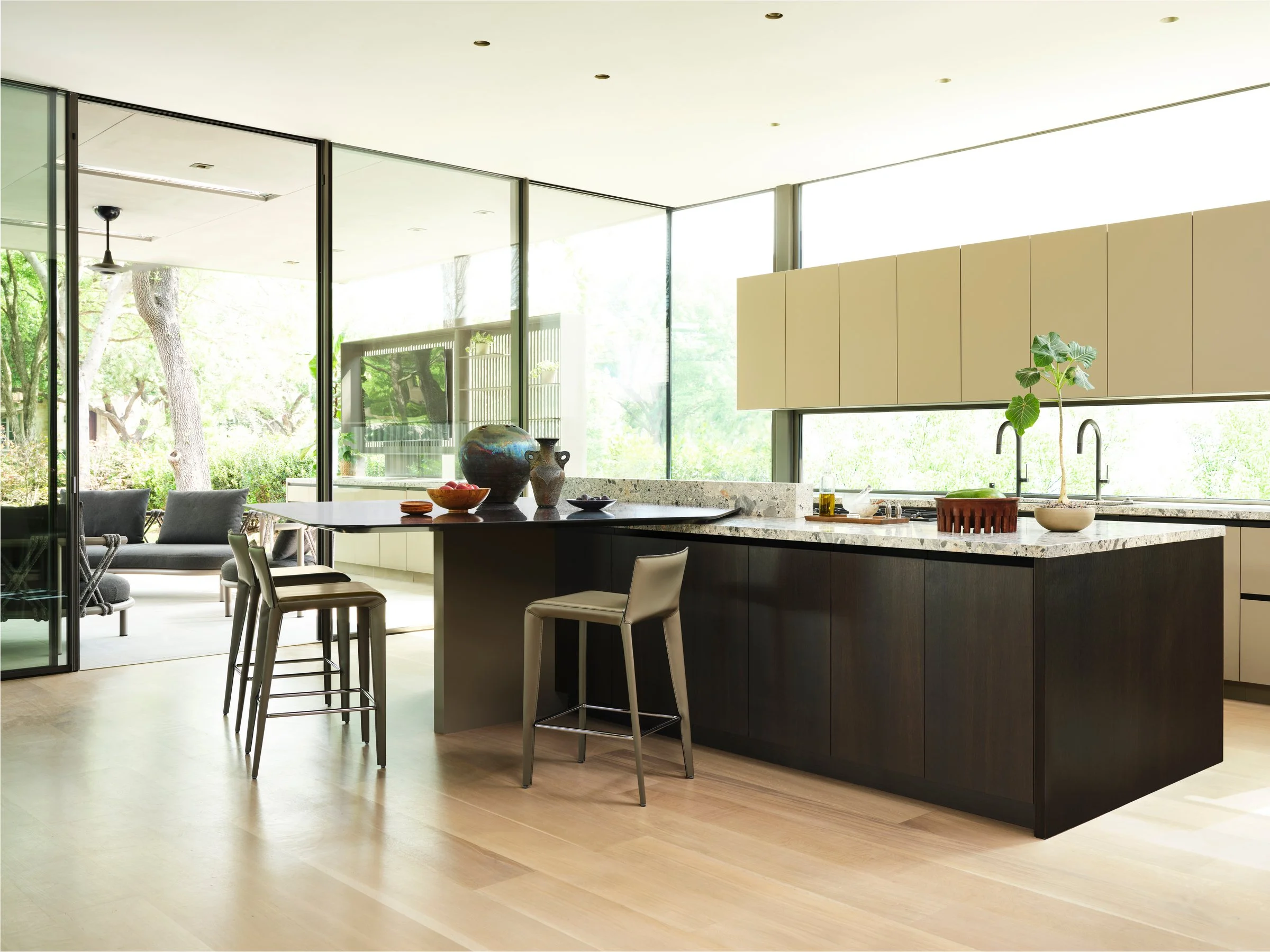 Modern kitchen with ceppo marble island, custom fumed oak wood cabinetry, and floor-to-ceiling glass, emphasizing material contrast and indoor-outdoor continuity.