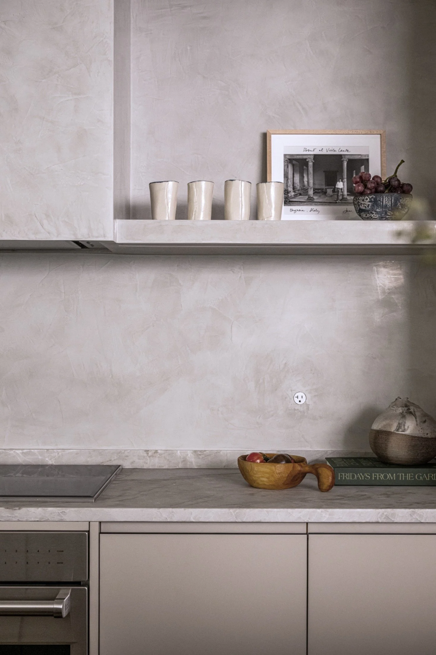 Minimalist kitchen with plaster walls, stone countertops, and open shelving styled with ceramics and artwork in a refined modern interior design.
