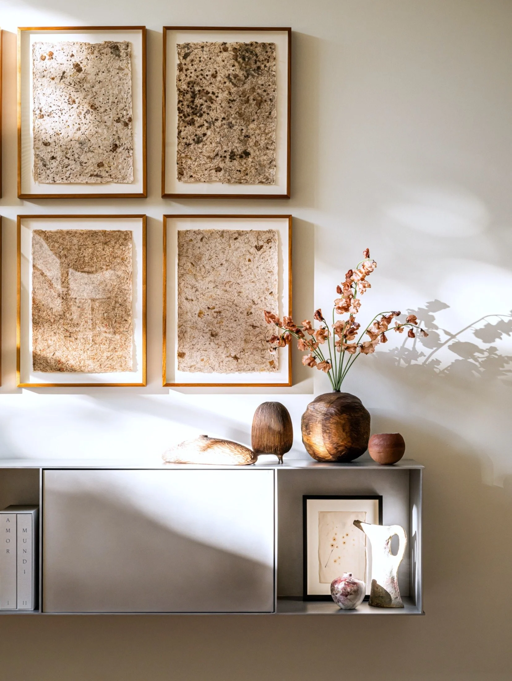 Modern waxed aluminum console by Jonathan Nesci with framed textured artwork, ceramic vessels, and natural materials, showcasing curated styling in a contemporary interior.