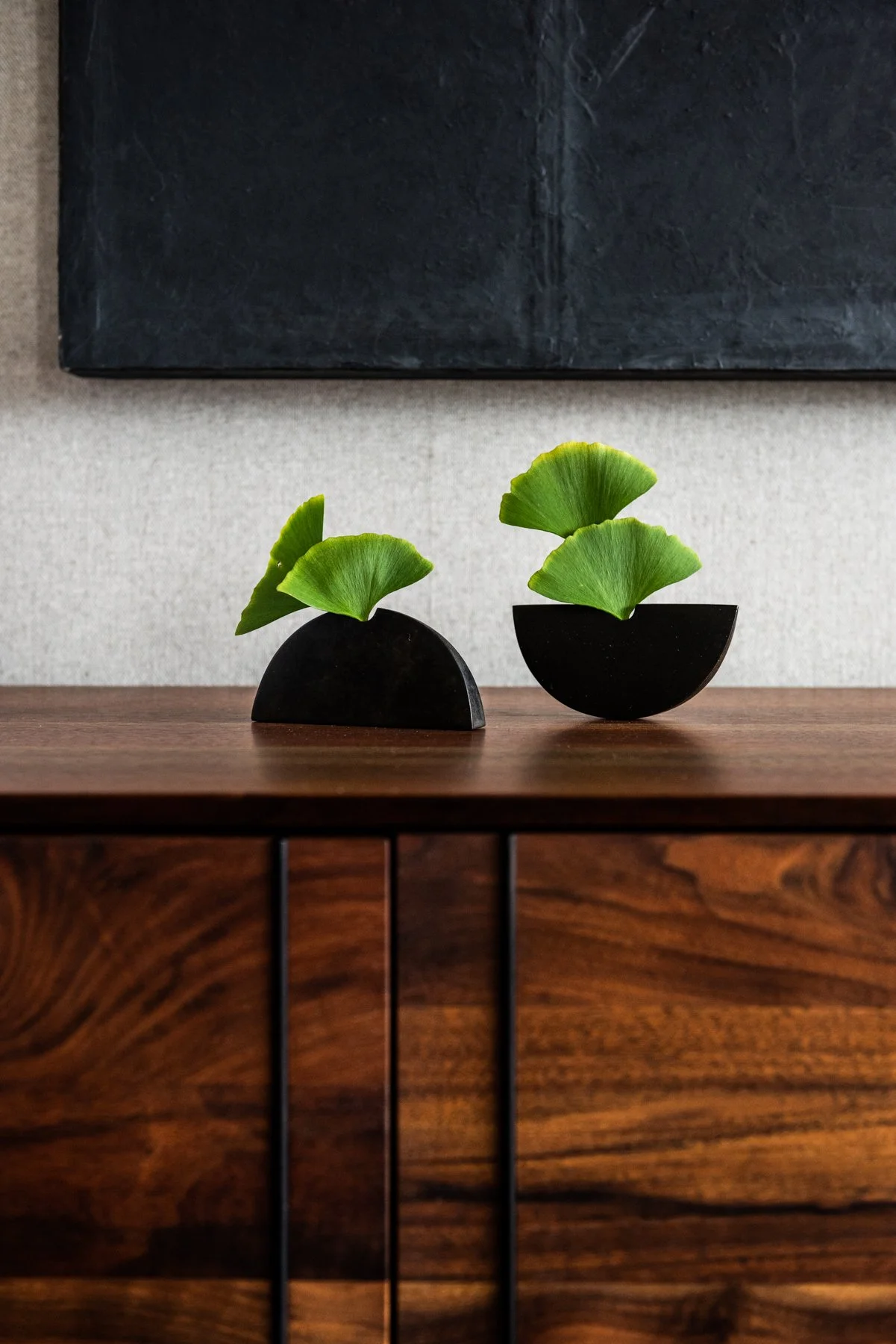 Minimal sculptural black bronze vessels by sakul Intakul with ginkgo leaves on walnut BDDW cabinet in modern interior styling