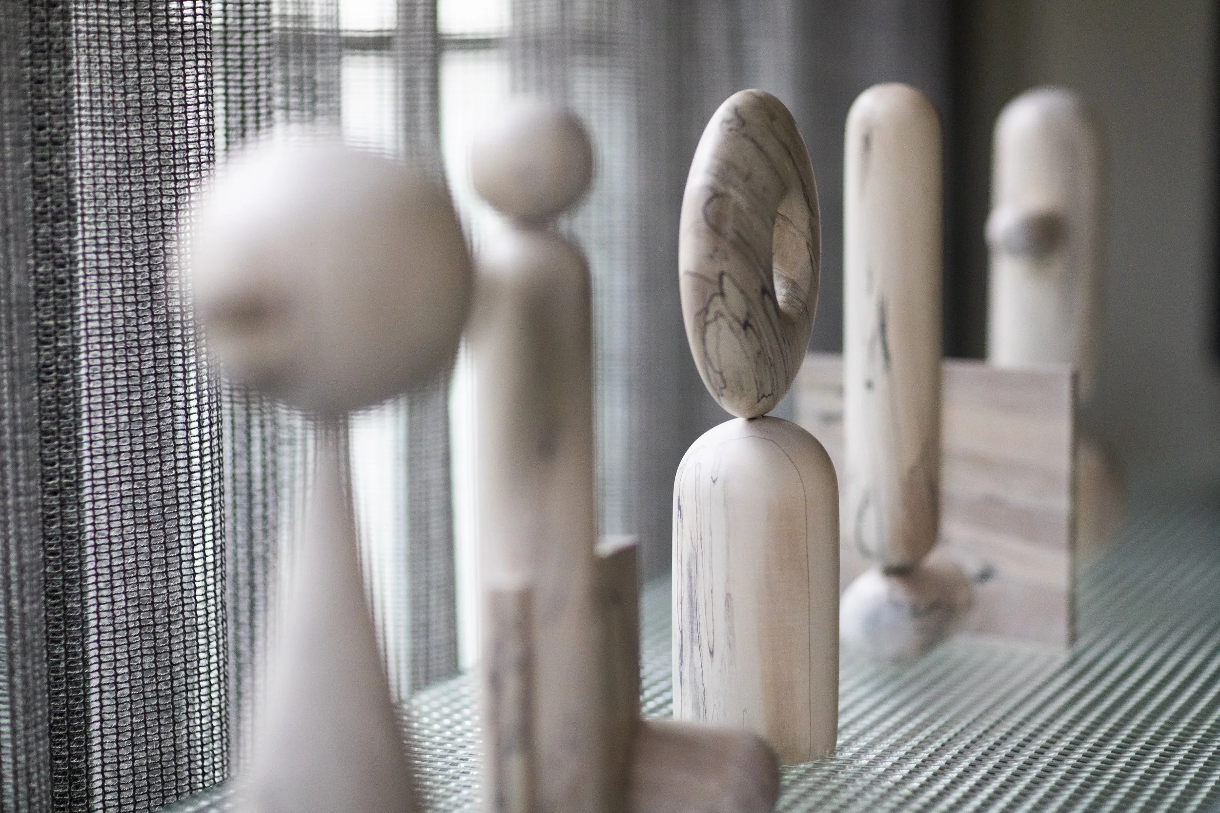 Carved maple sculptural objects displayed on textured glass cabinet with sheer linen drapery hamilton holmes glas italia