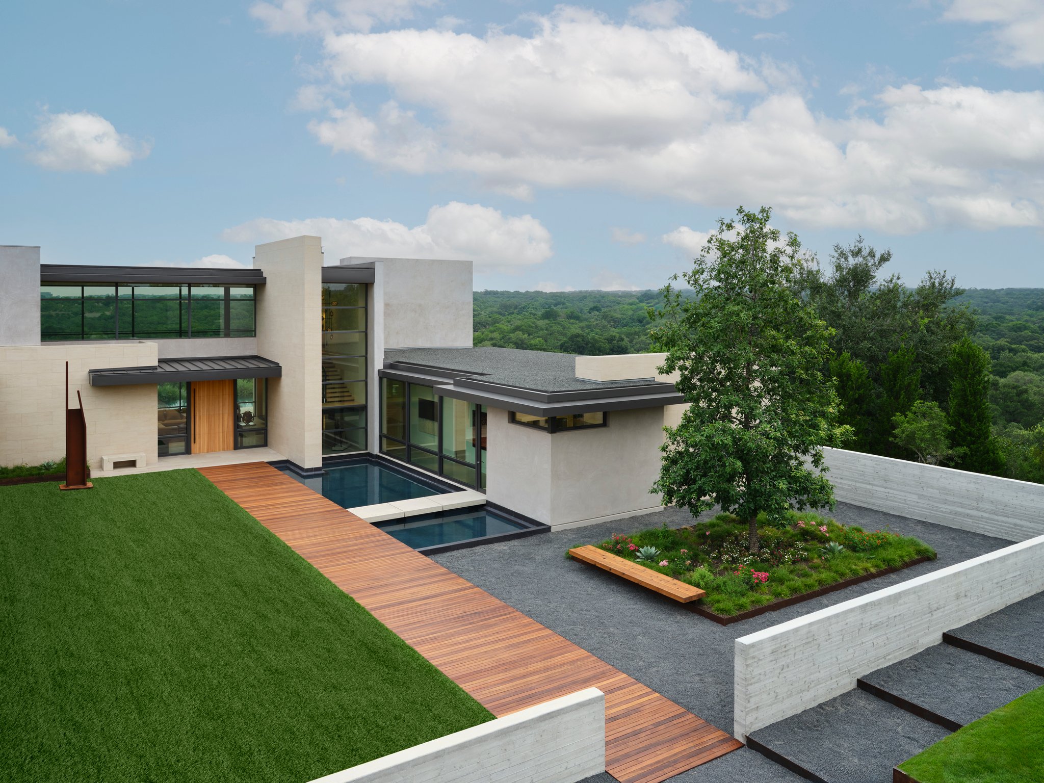 Elevated view of a contemporary courtyard garden with wood bridge entry, reflecting pool, and structured landscape planting set against limestone architecture.