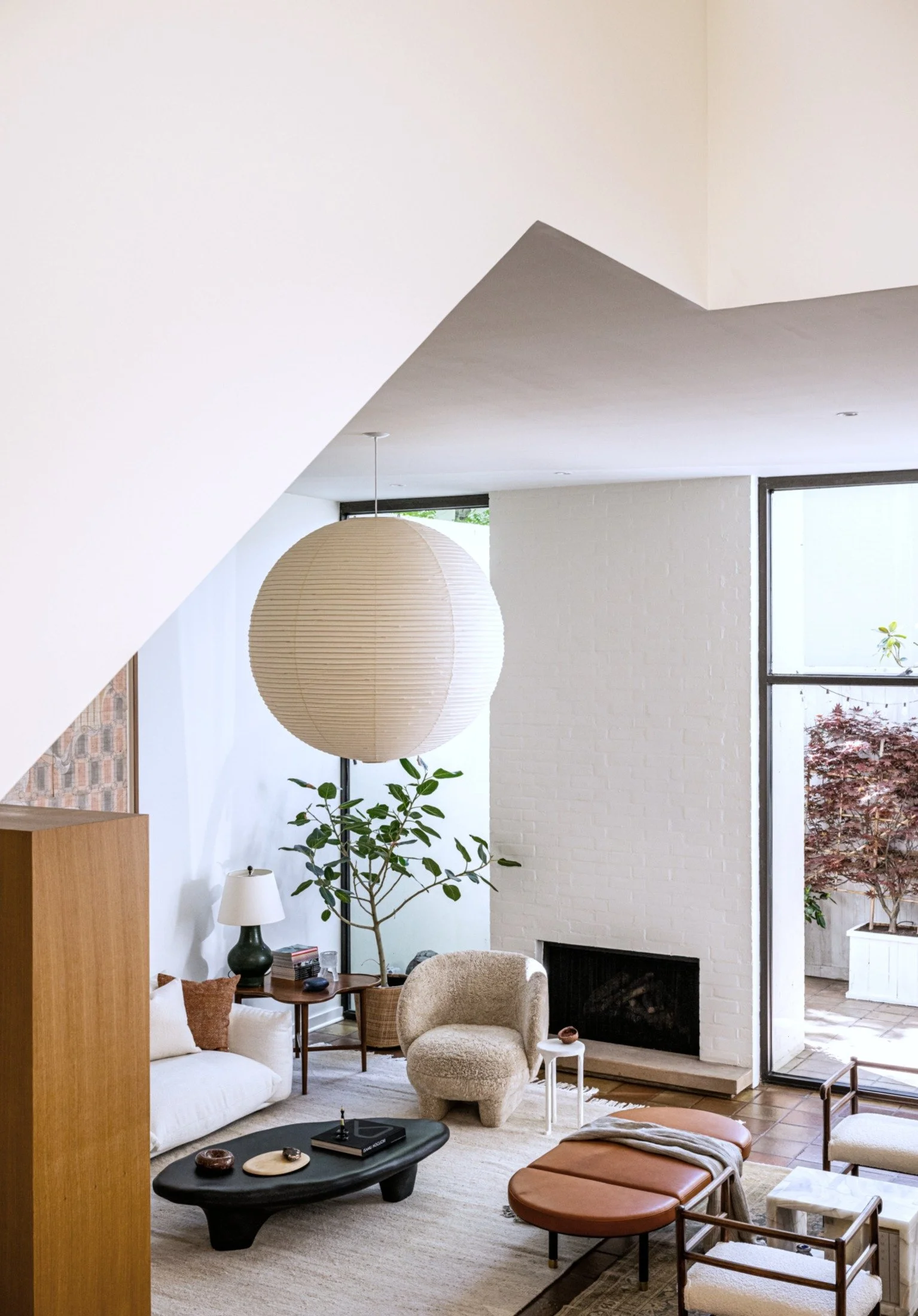 Modern living room with sculptural furniture, Akari Noguchi paper lantern pendant, and fireplace, blending soft textures and natural materials in a contemporary residential interior.