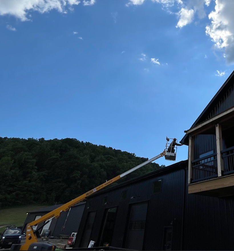 Utility lift extended to the second floor of a dark building, with a background of a blue sky with some clouds and a green hillside.