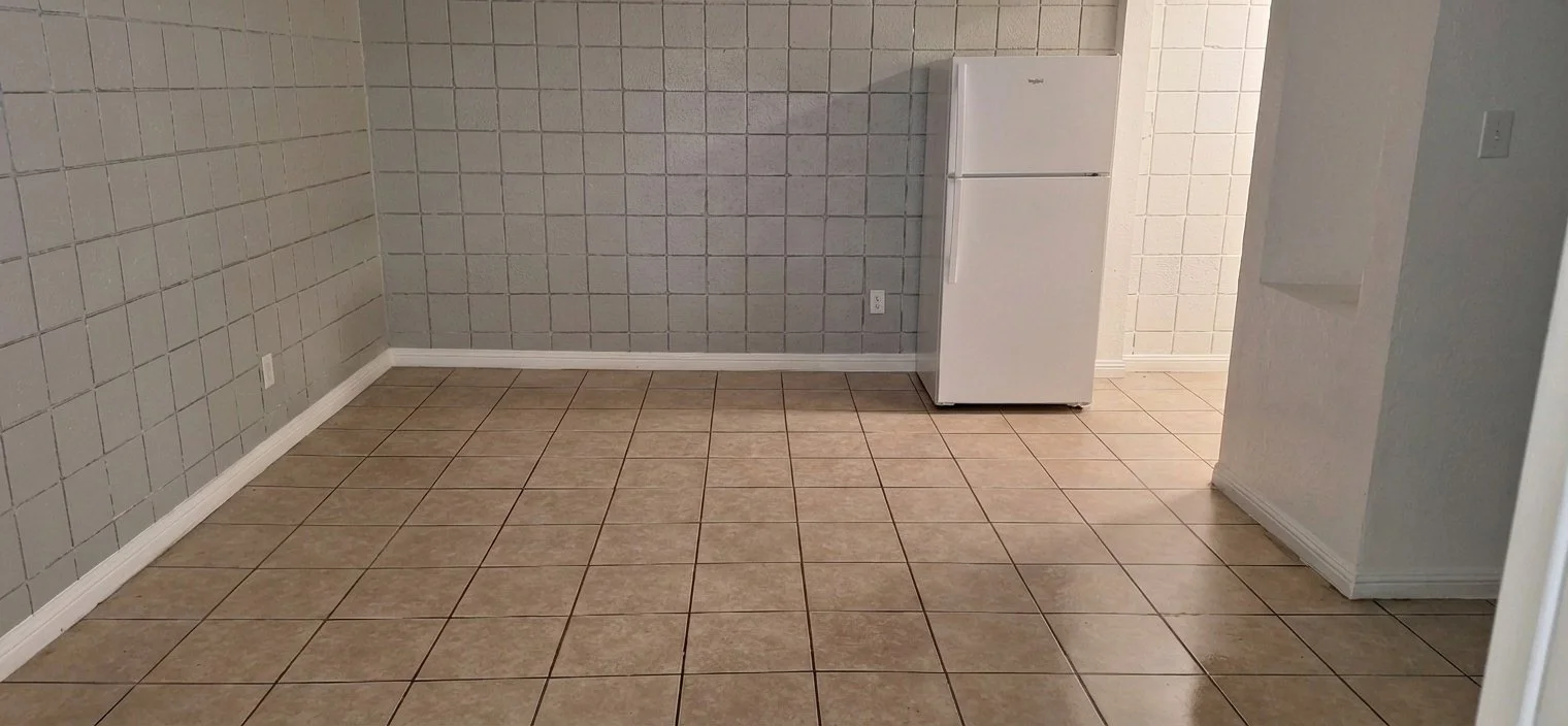 Empty tiled room with a white refrigerator near the back wall.