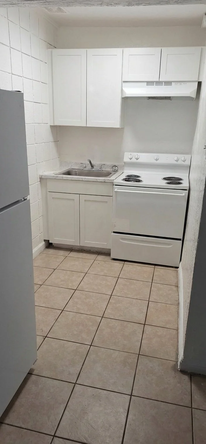 Small kitchen with white cabinets, a sink, a white stove, and beige tiled floor.