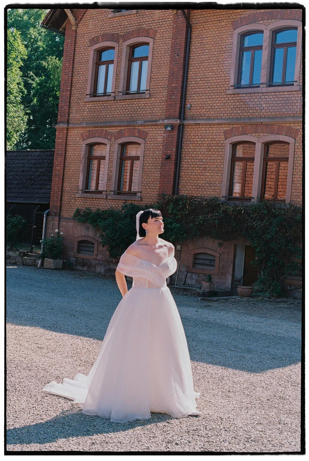 Eine Frau in einem weißen Brautkleid steht vor einem roten Backsteingebäude im Freien.