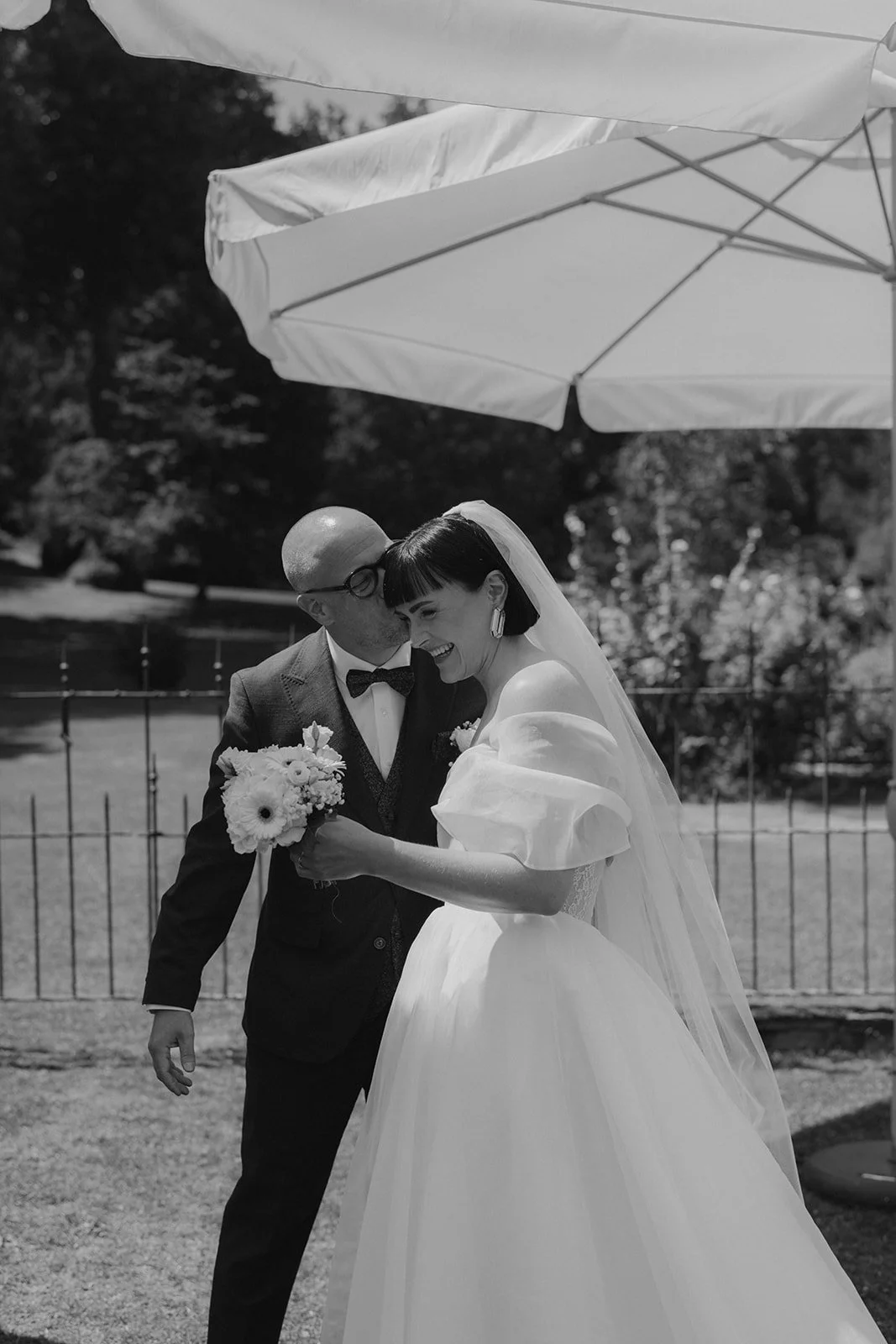 Braut und Bräutigam bei ihrer Hochzeit, lachen unter einem weißen Sonnenschirm im Freien während ihrer freien Trauung auf dem Gutshof unterbessenbach bei Frankfurt am main