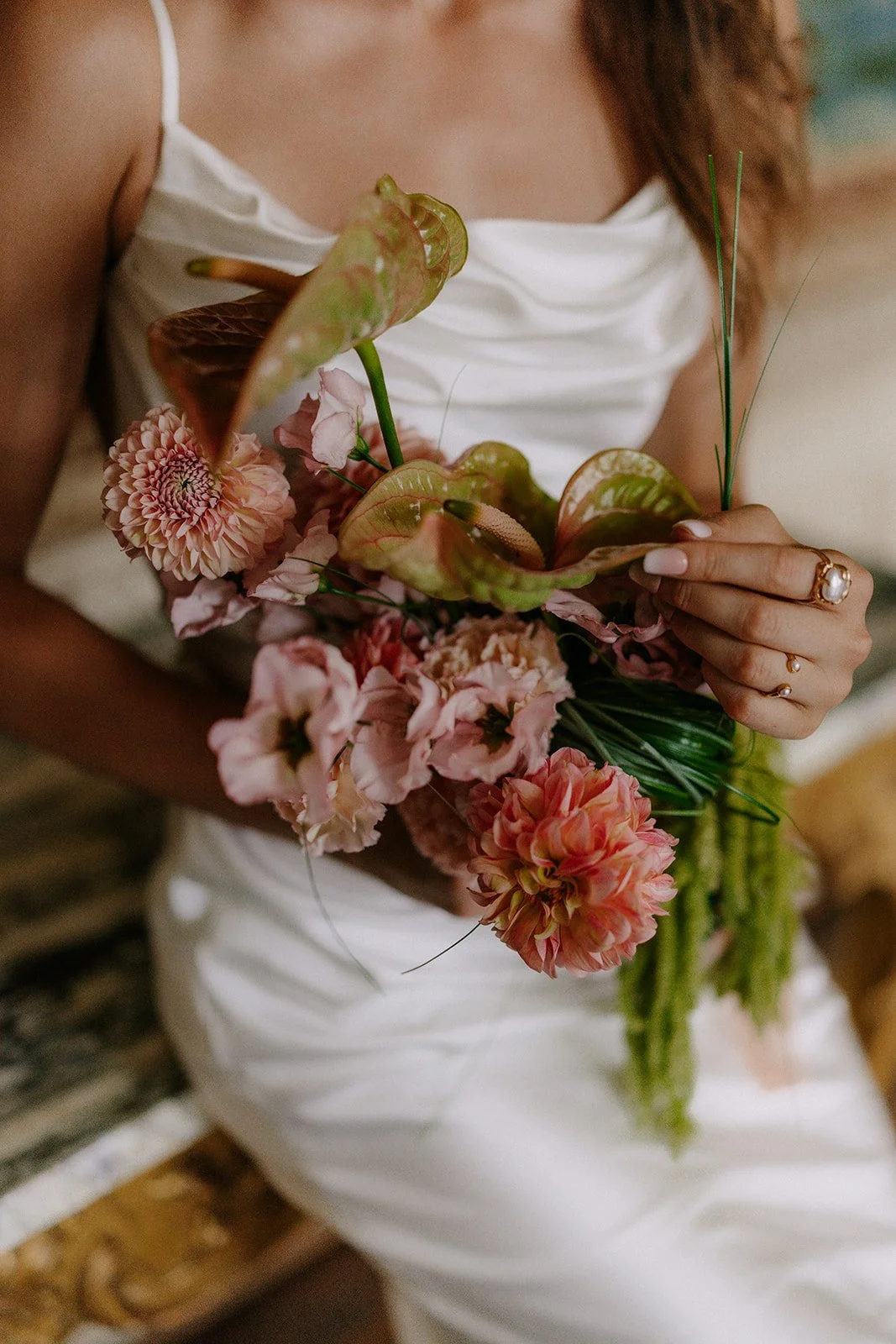 Braut trägt weiße Kleid und hält einen Blumenstrauß mit rosa und roten Blumen und grünen Blättern.