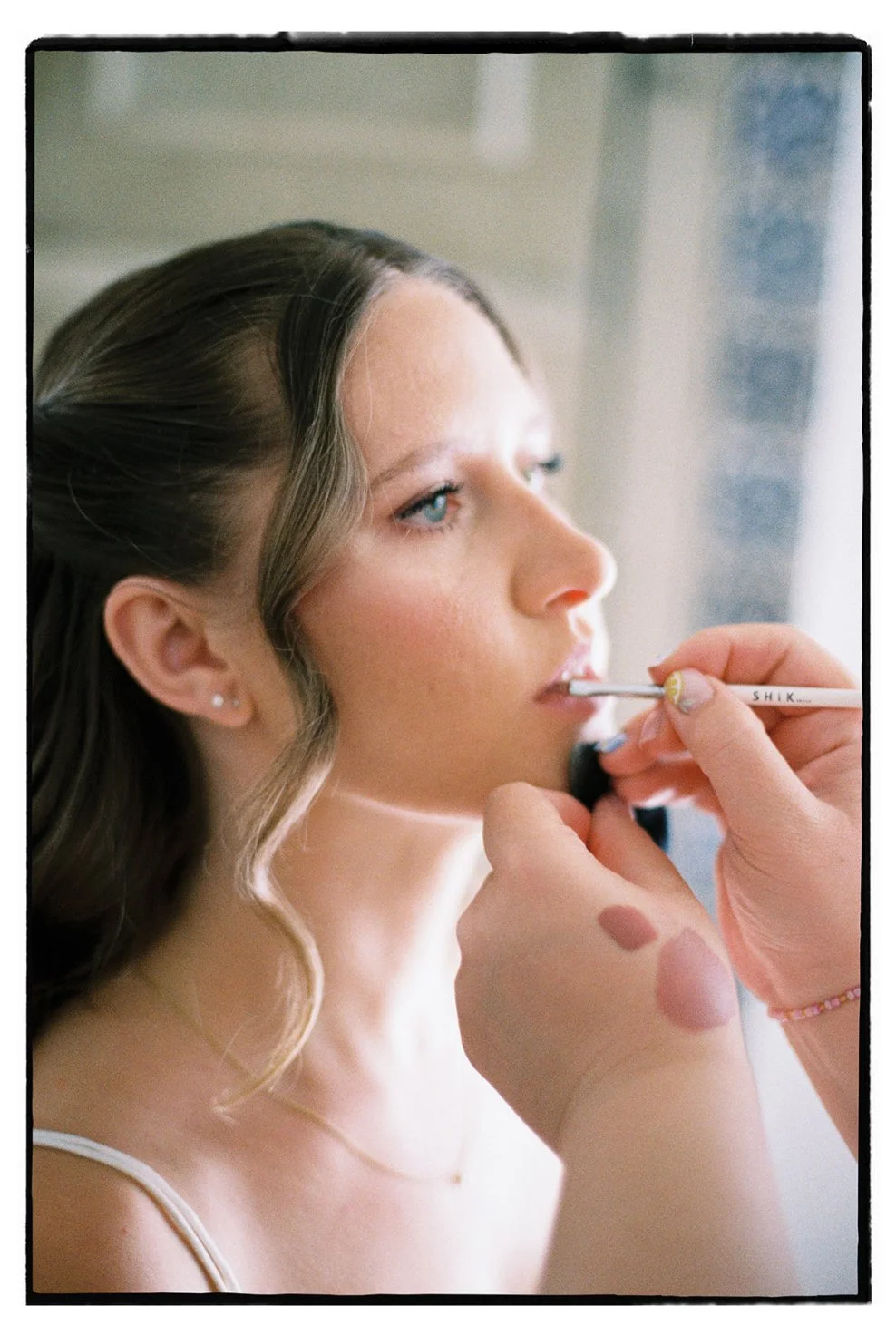 Eine Frau erhält Make-up, während sie sich ansieht. Der Fokus liegt auf ihrem Gesicht und dem Make-up-Pinsel.