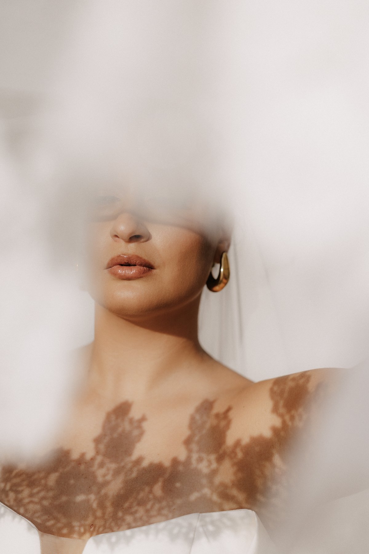 Ein Model mit goldenen Ohrringen und natürlichem Make-up, teilweise von einer weißen, unscharfen Oberfläche bedeckt.