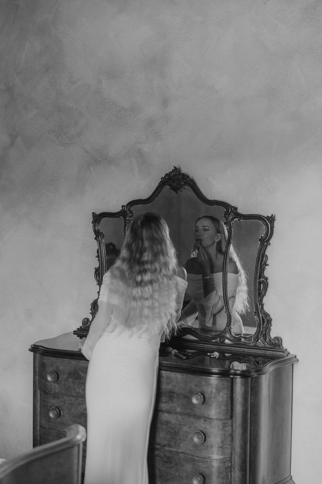 Frau macht sich im Badezimmer fertig, schaut in den Spiegel, das Bild ist schwarz-weiß.