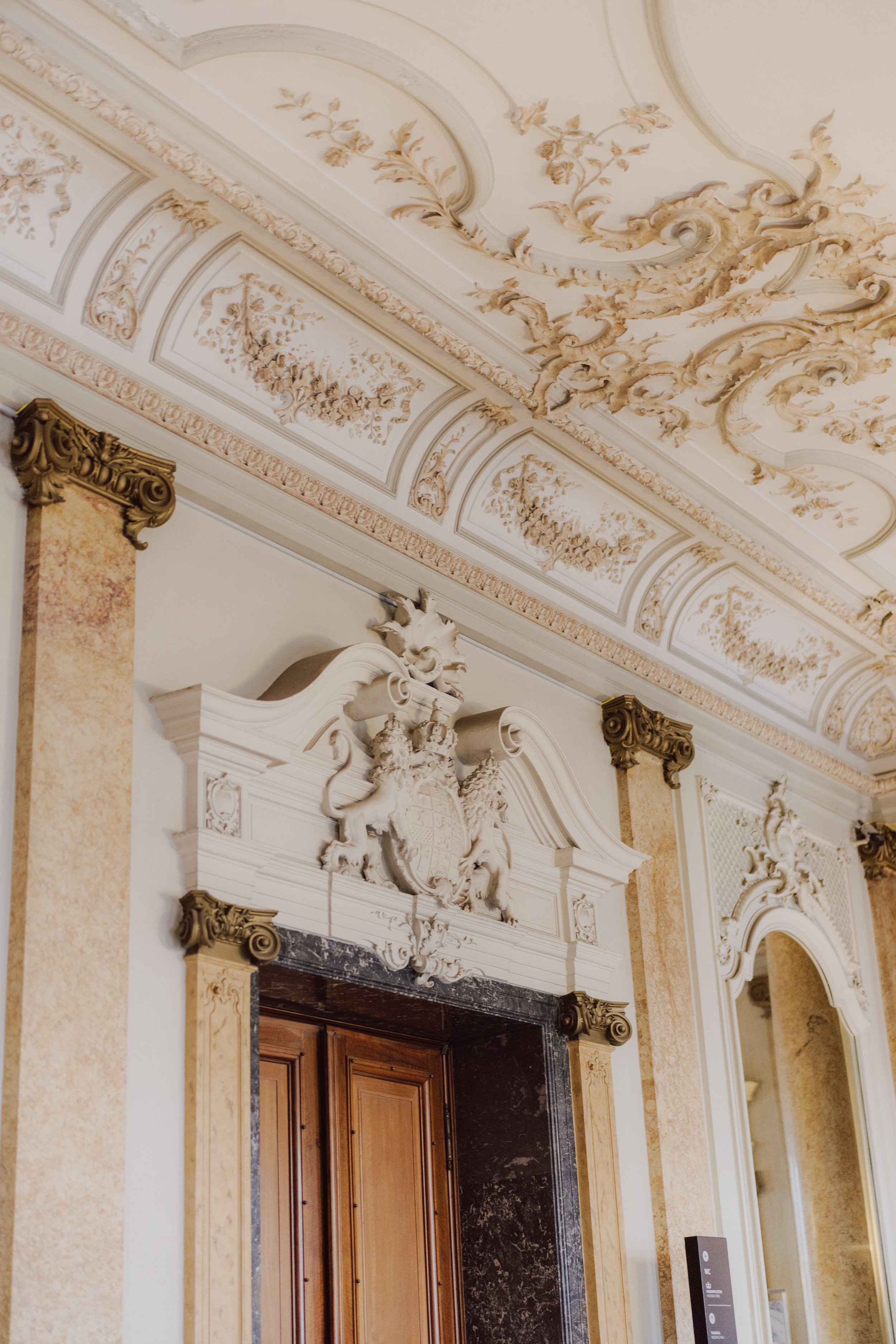 Die Decke und der obere Bereich eines Eingangsbereichs mit kunstvollen Stuckarbeiten und Verzierungen in einem eleganten, historischen Gebäude.