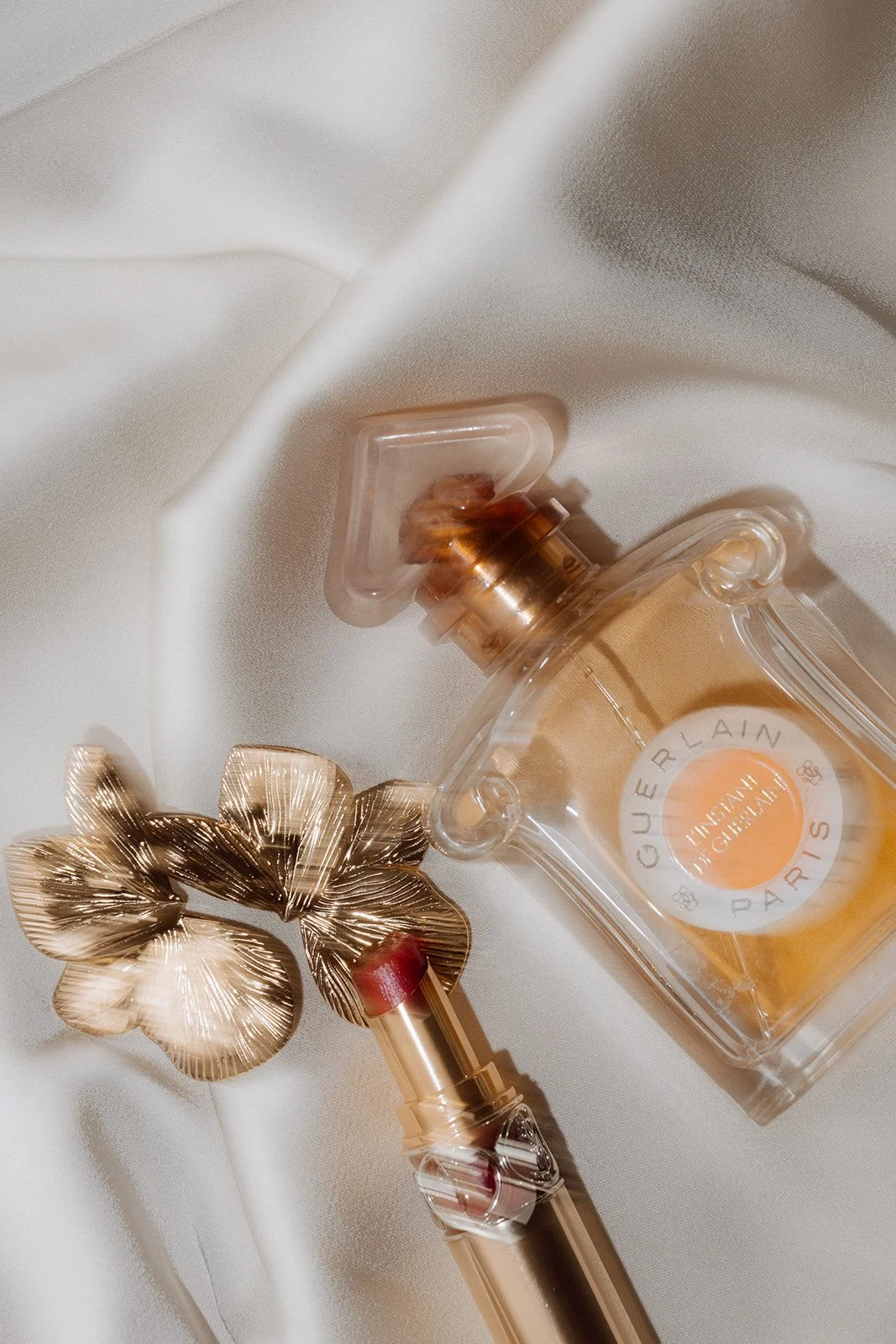 Flasche mit französischem Parfüm Guerlain und einem goldfarbenen Schmuckstück auf weißem Satin