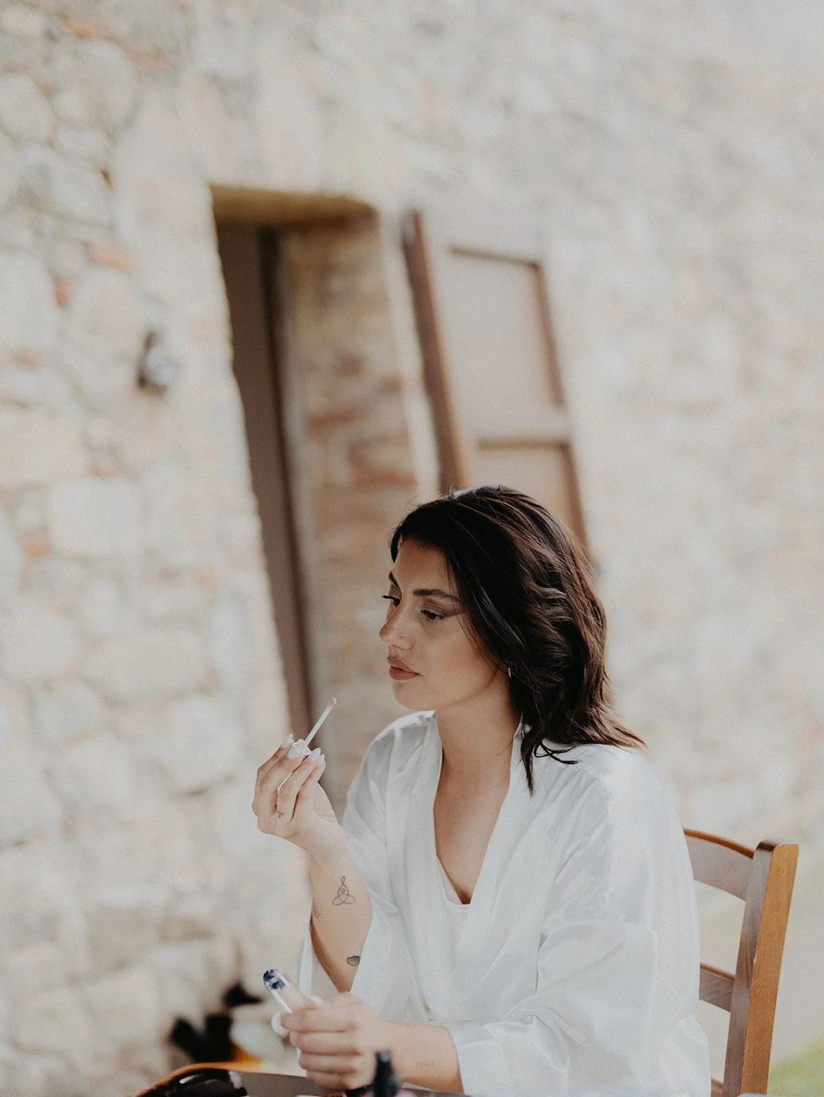 Eine Braut beim getting ready mit dunklen, schulterlangen Haaren und Tattoos auf den Armen, schminkt sich für ihre freie Trauung in Poggio covili in der Toskana bei ihrer destinationwedding