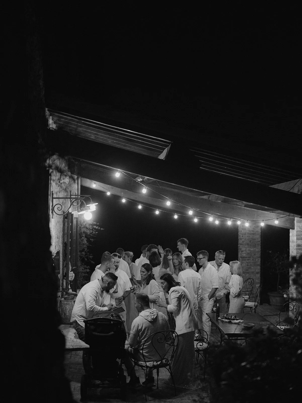 Menschen versammeln sich in einem dunklen Außenbereich mit Kronleuchtern und Lichterketten, viele tragen weiße Kleidung auf Poggio covili