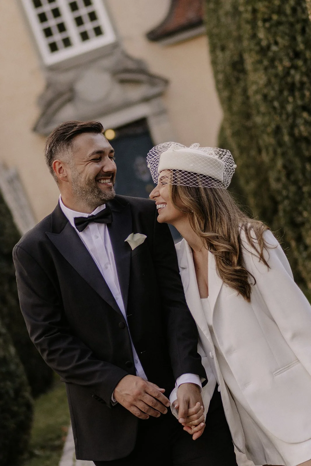 Ein glückliches HochzeitsPaar, vermutlich Braut und Bräutigam, hält Händchen vor einem historischen Gebäude, lächelt sich liebevoll an, bei einer zivilen Trauung in Zürich Küsnacht.