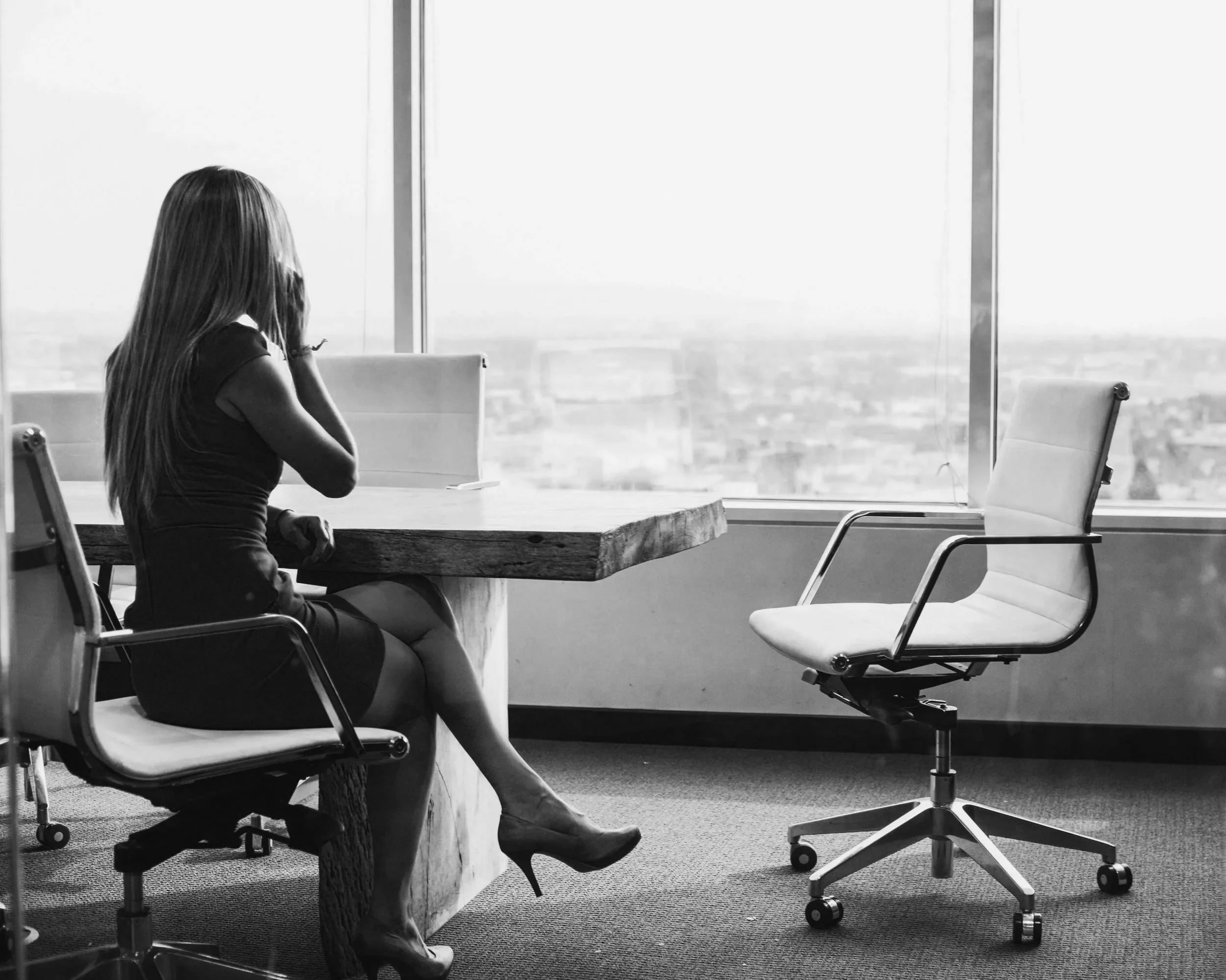 Female executive on her cell phone at a conference room desk with an empty chair next to her calling someone