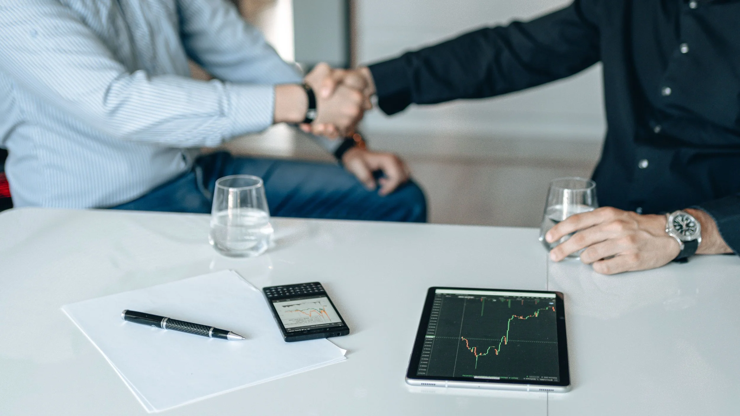Two business people giving a supportive handshake with financial data on the table