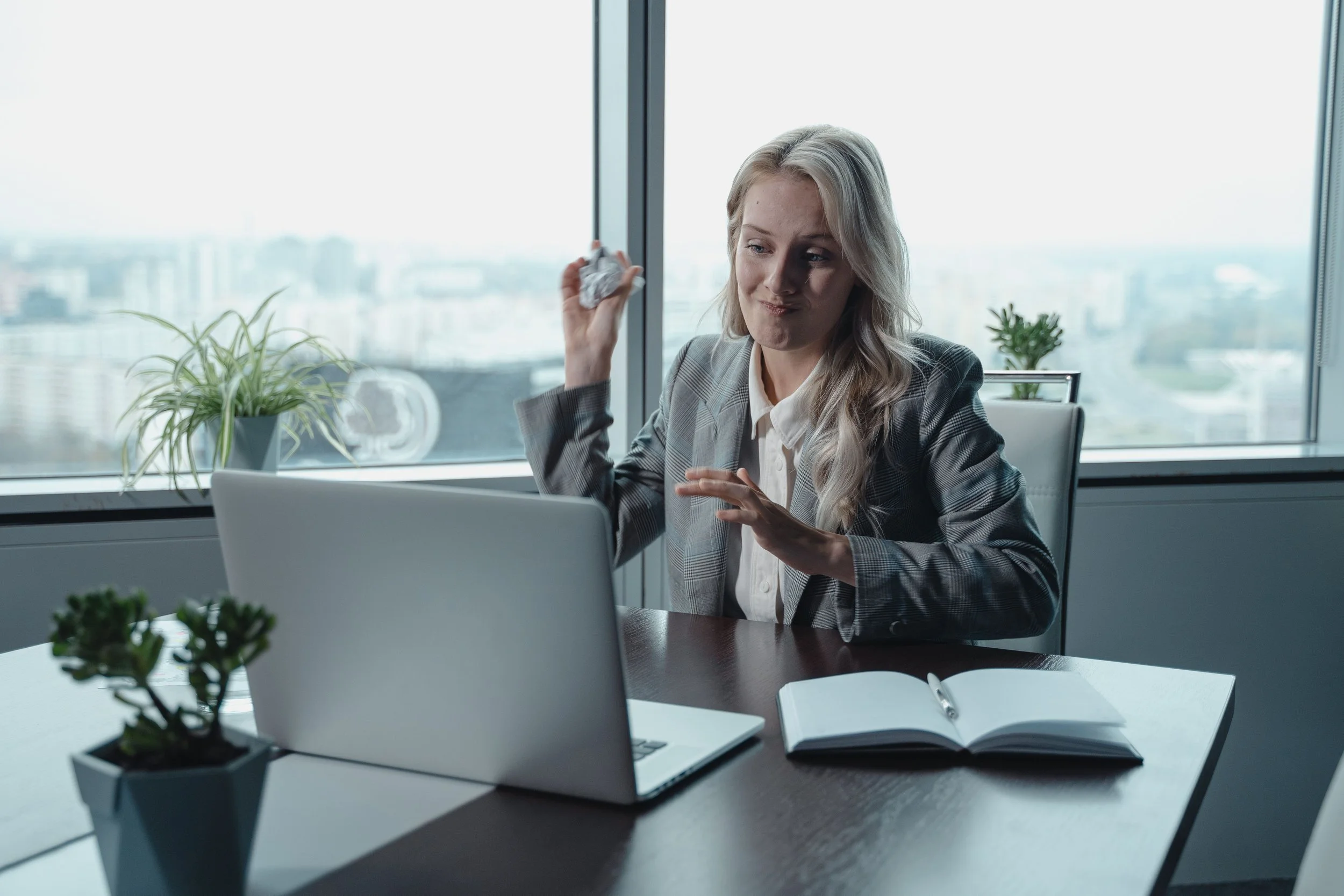 frustrated woman throwing a bunched up piece of paper at her laptop in a office
