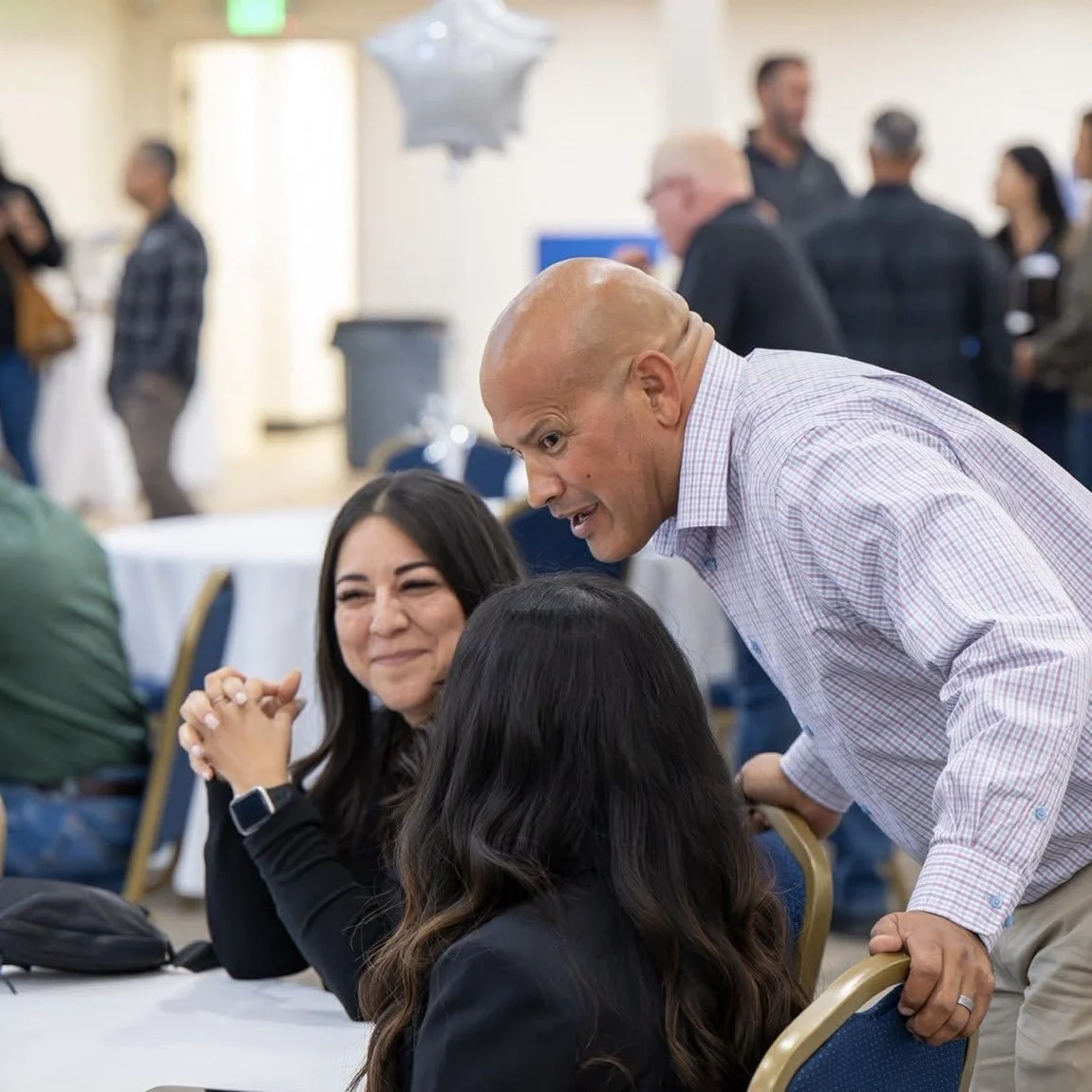 Luis Lara and two women engaged in conversation at a social gathering, with other people in the background.
