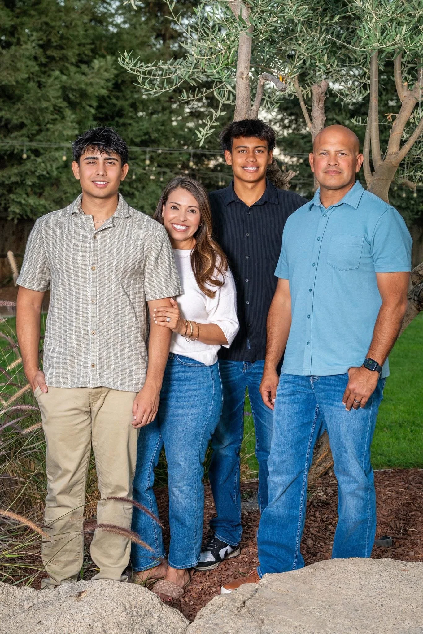 The Lara family standing outdoors in front of trees and greenery, smiling at the camera.