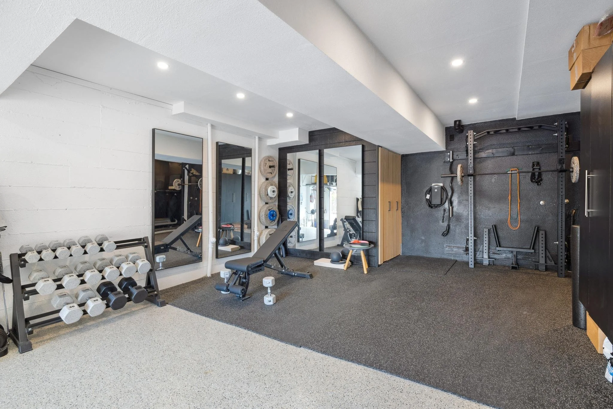 Home gym with dumbbell rack, weight bench, mirrors, and strength training equipment in a modern basement