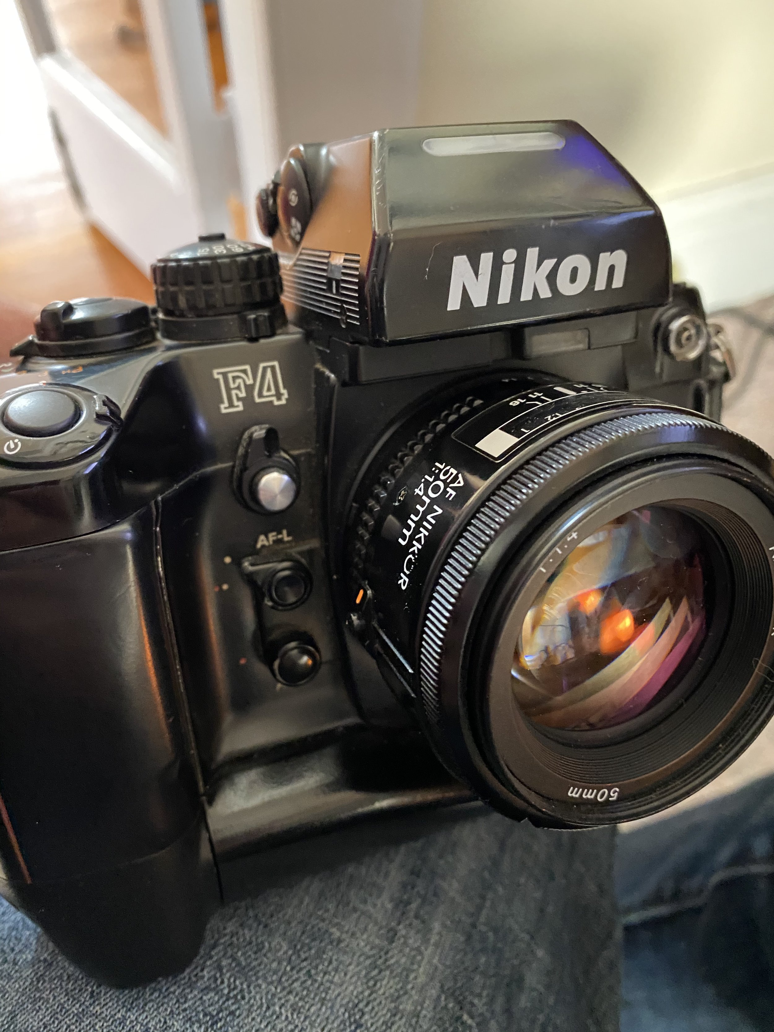 A Sony F4 camera with a Nikon lens attached, showing various controls and dials, positioned on someone's lap with a blurred background.