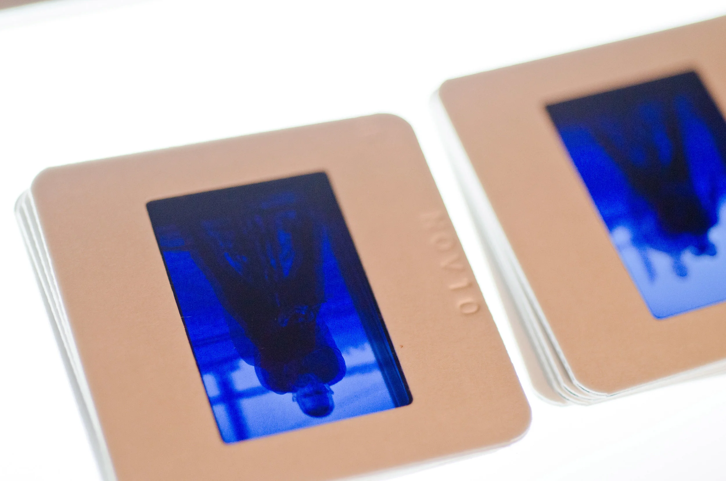 Close-up of two Polaroid-style photographs with blue-tinted images of a person with short hair and a dark shirt, one photograph slightly overlapping the other.