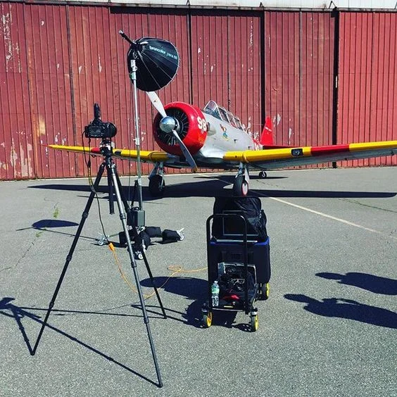 A vintage aircraft positioned outdoors with camera and lighting equipment set up around it for a photo shoot.
