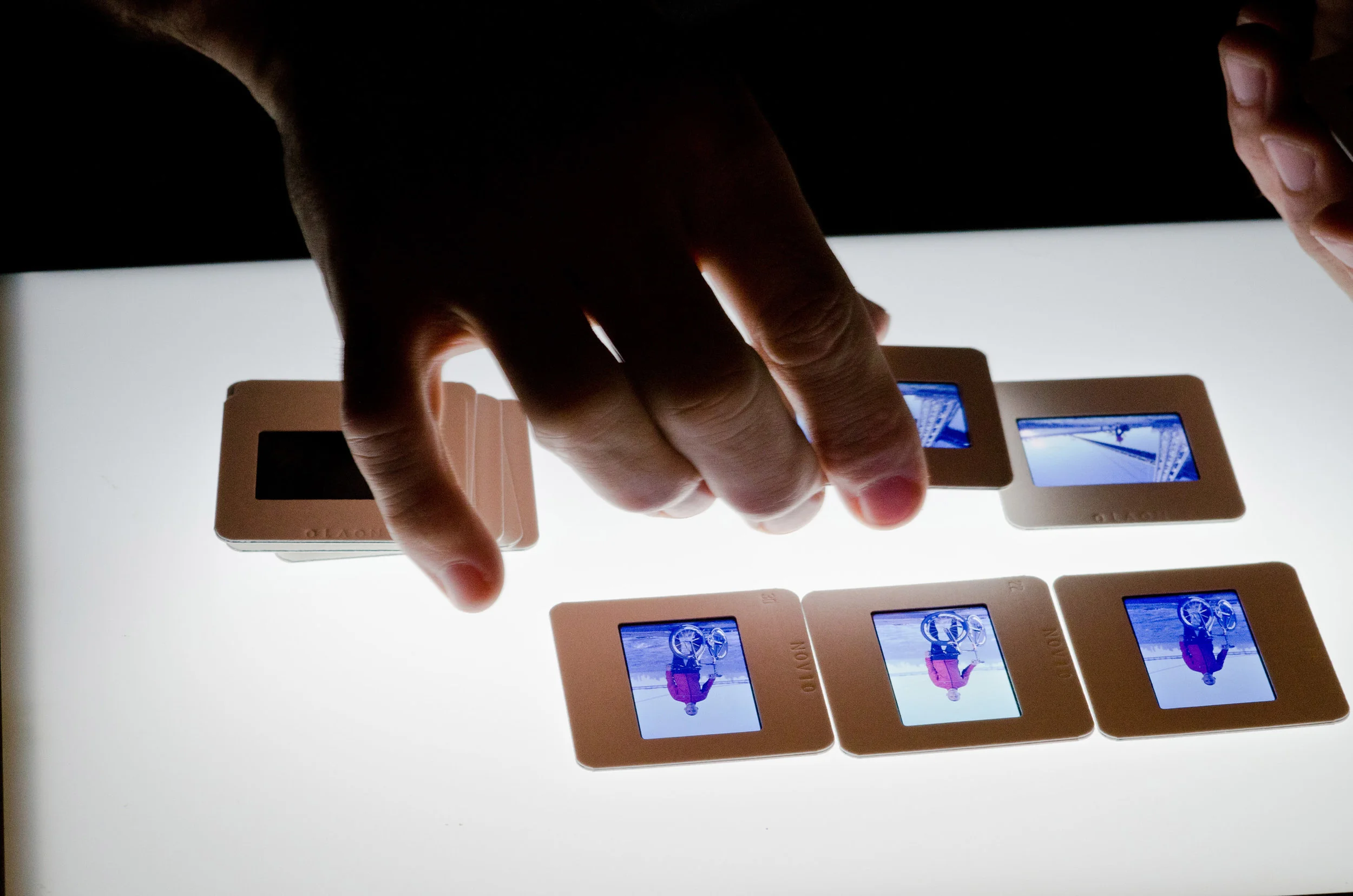 Hand flipping the slides of a film strip with images of people skateboarding at an outdoor skate park on a sunny day.