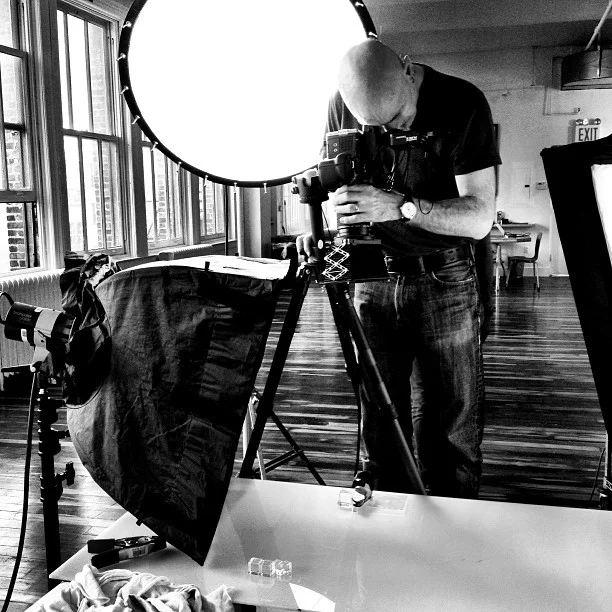 Photographer setting up camera and lighting equipment in a studio with large windows.