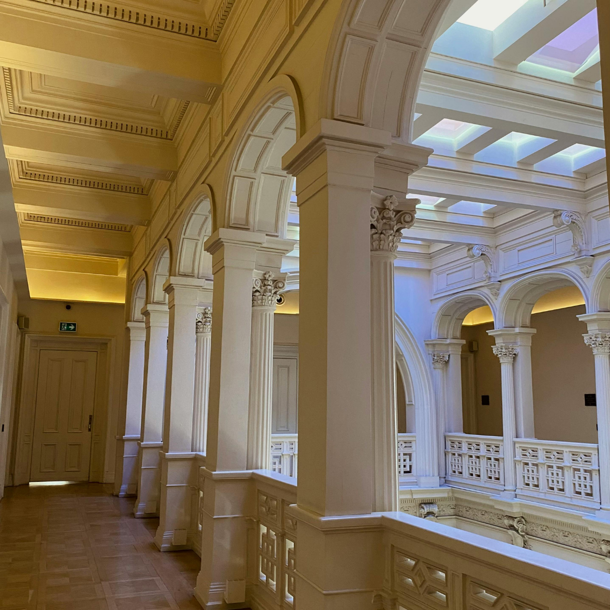 Interior view of a building with classical architecture, featuring white columns with intricate capitals, arched windows, and a ceiling with skylights.