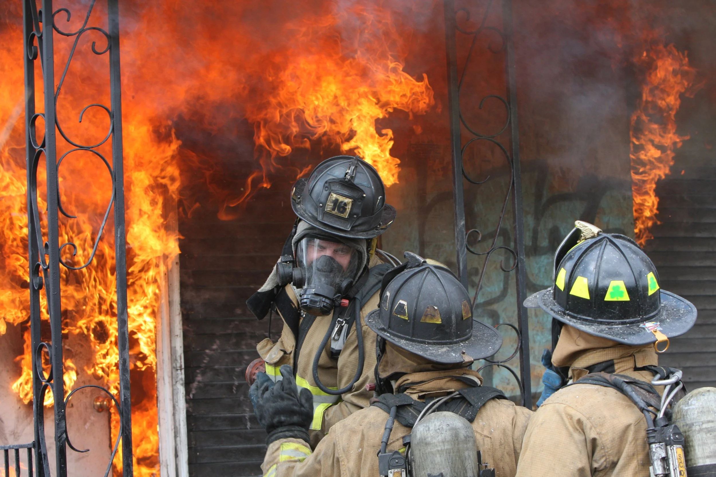 Firefighters battling a house fire with flames and smoke coming out of a burning building.